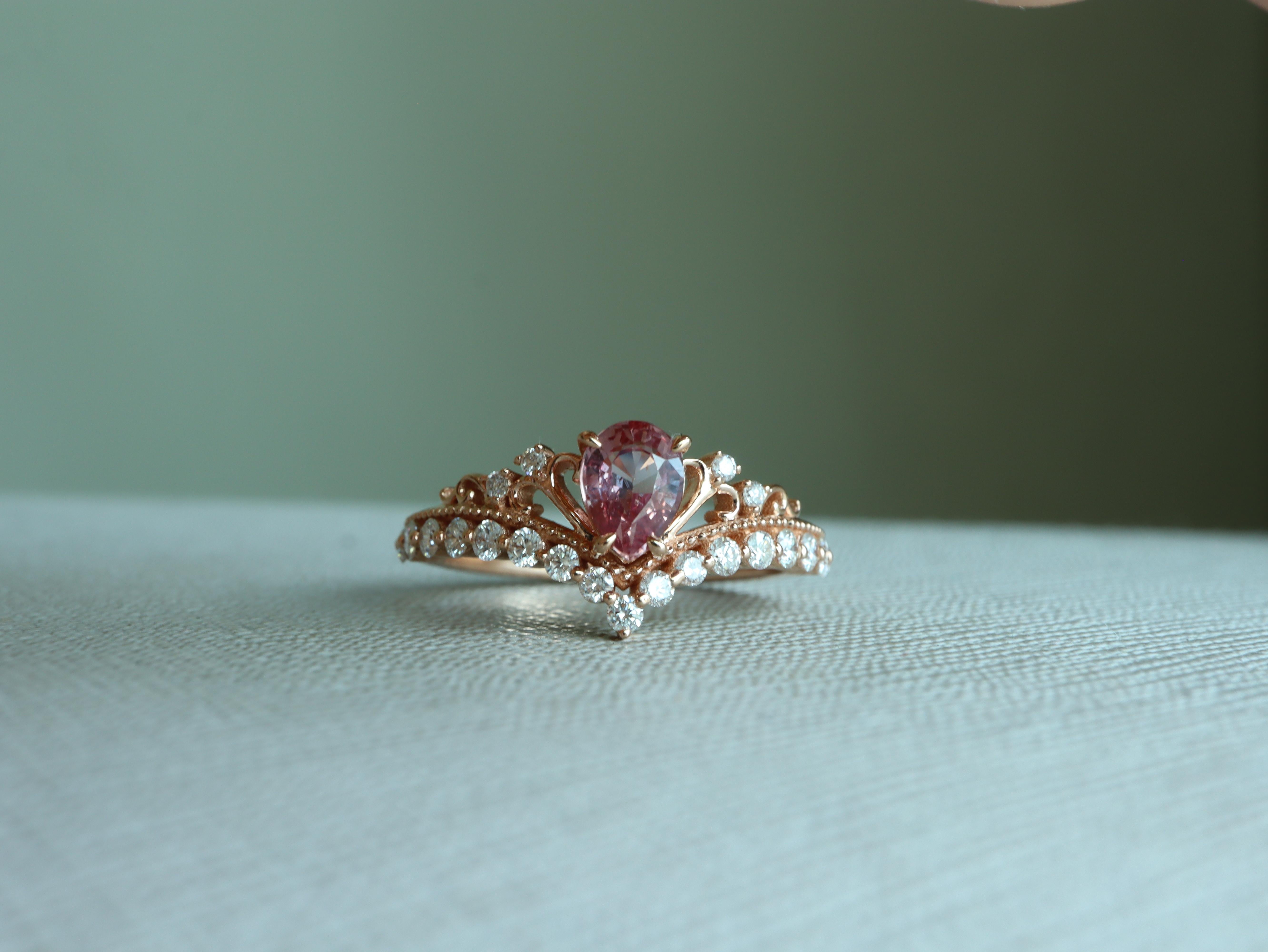Der Padparadscha-Saphir ist als einer der seltensten Edelsteine der Welt bekannt. Dieser Tiara-Kronenring ist sorgfältig aus massivem 18-karätigem Gold gefertigt und zeigt in der Mitte einen No Heat Padparadscha, der durch schimmernde natürliche