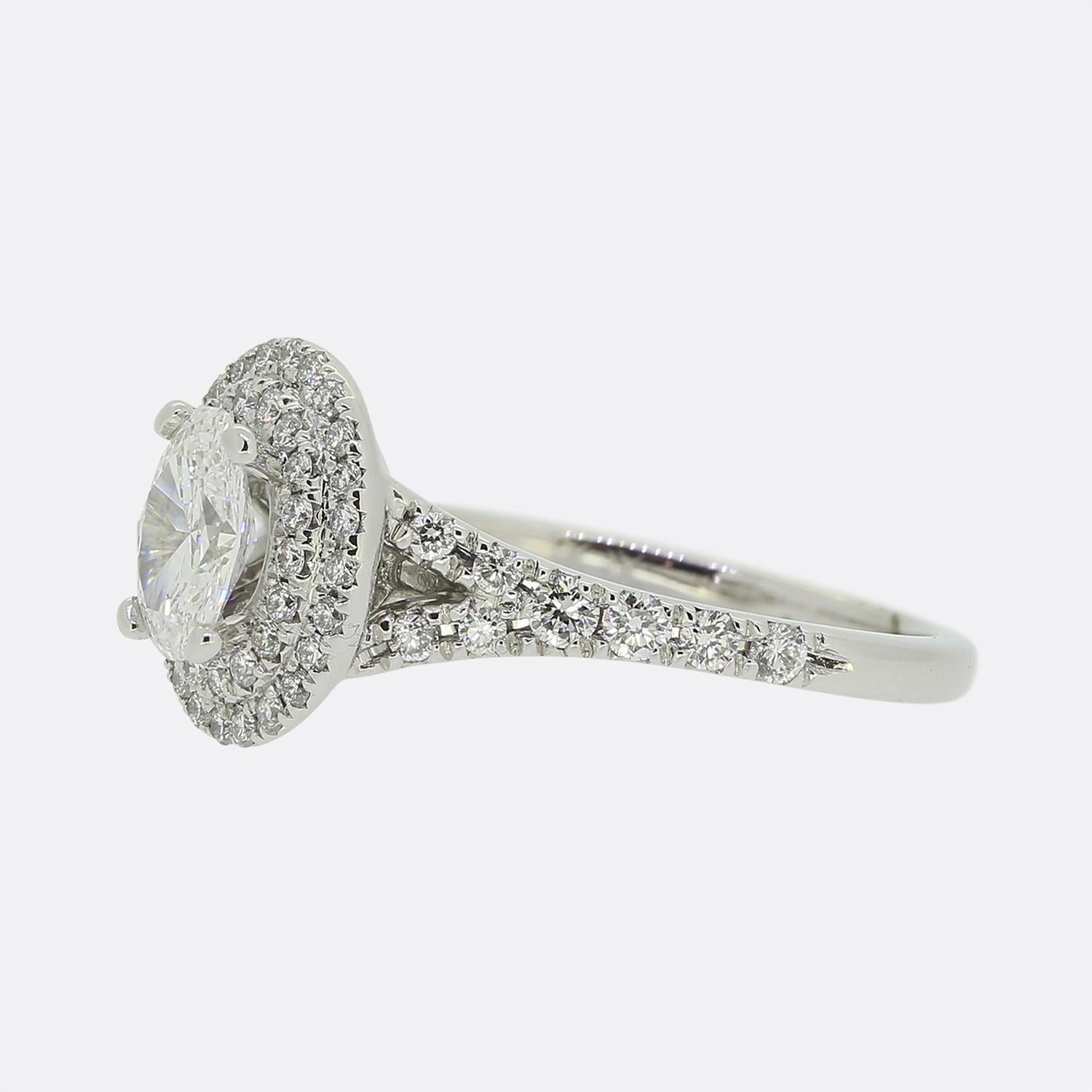 Ecco uno splendido anello di fidanzamento con diamante. Questo gioiello in oro bianco 18 ct ospita un singolo diamante ovale sfaccettato incastonato in una montatura a 4 griffe al centro del quadrante. Questa pietra principale è poi circondata da