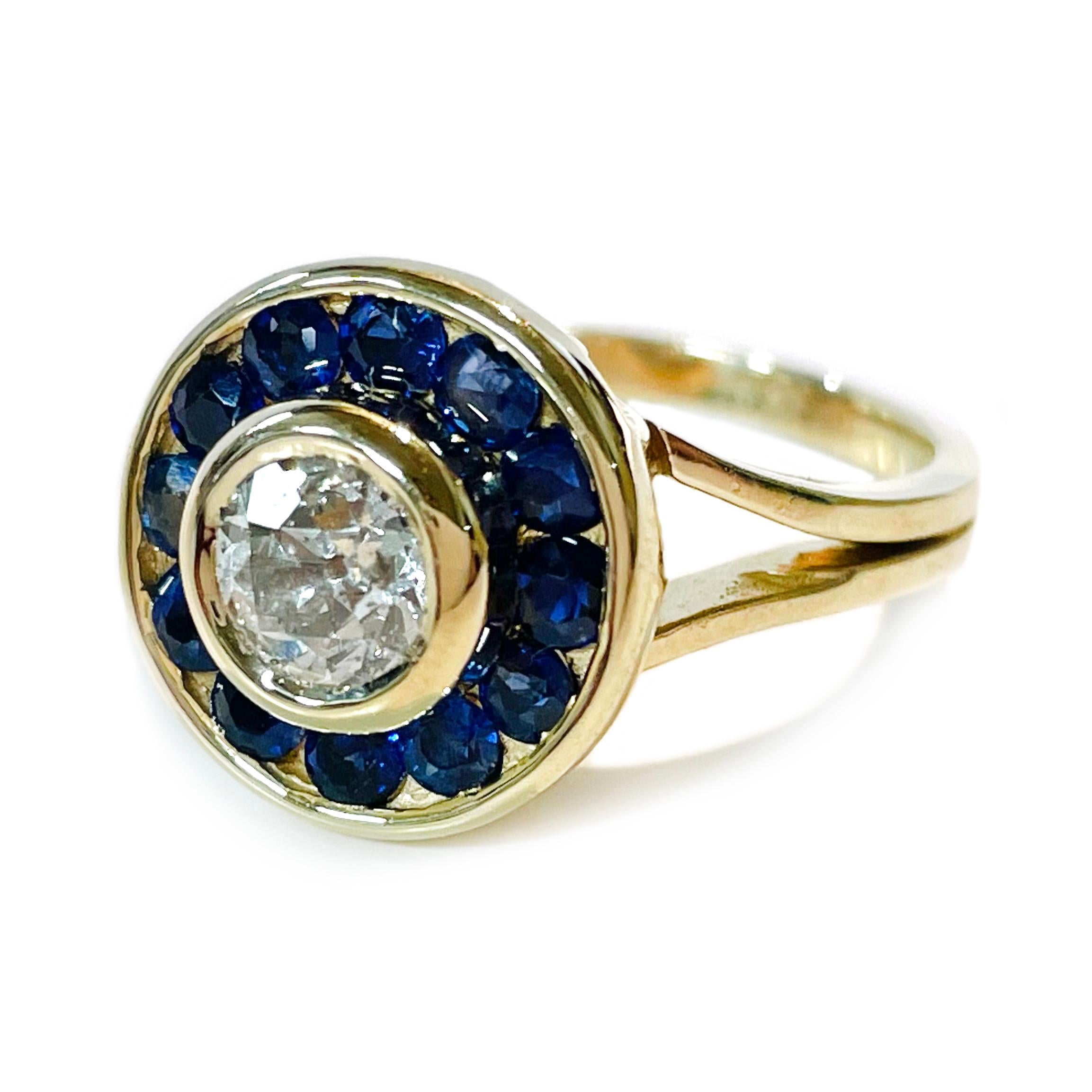 14 Karat Euro-Cut Diamond Blue Sapphire Ring. The ring features a center bezel-set 5.6mm Euro-cut round diamond with a carat weight of 0.65ct and twelve channel-set 3.2mm round blue sapphires with a total carat weight of 0.72ctw. The diamond is