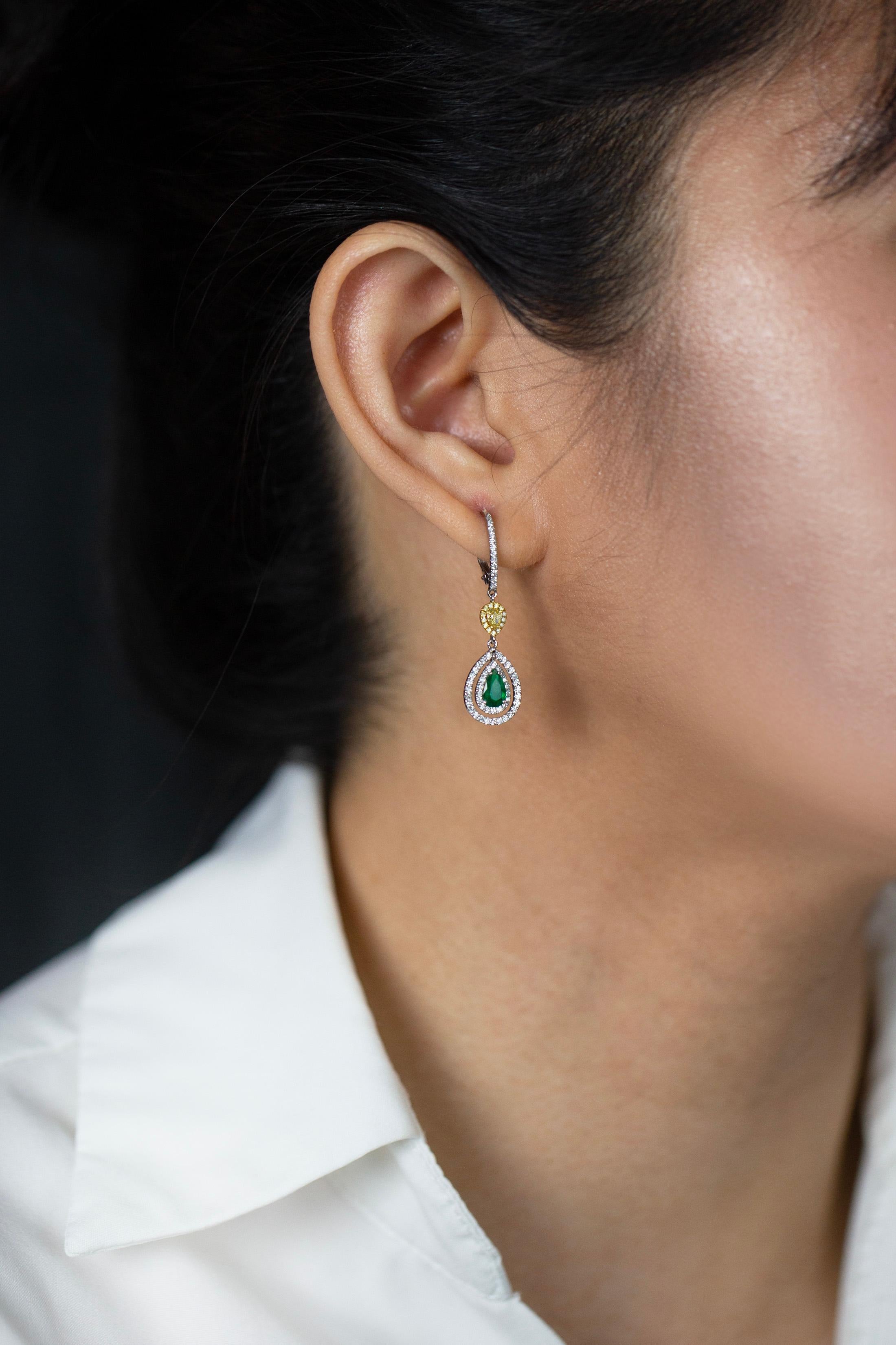 Showcasing an elegant dangle earrings set with 2 pear shape green emeralds weighing 0.69 carats total. The emeralds are surrounded by 2 rows of brilliant round diamonds and suspended on an accented lever-back weighing 0.57 carats total. Spaced by a