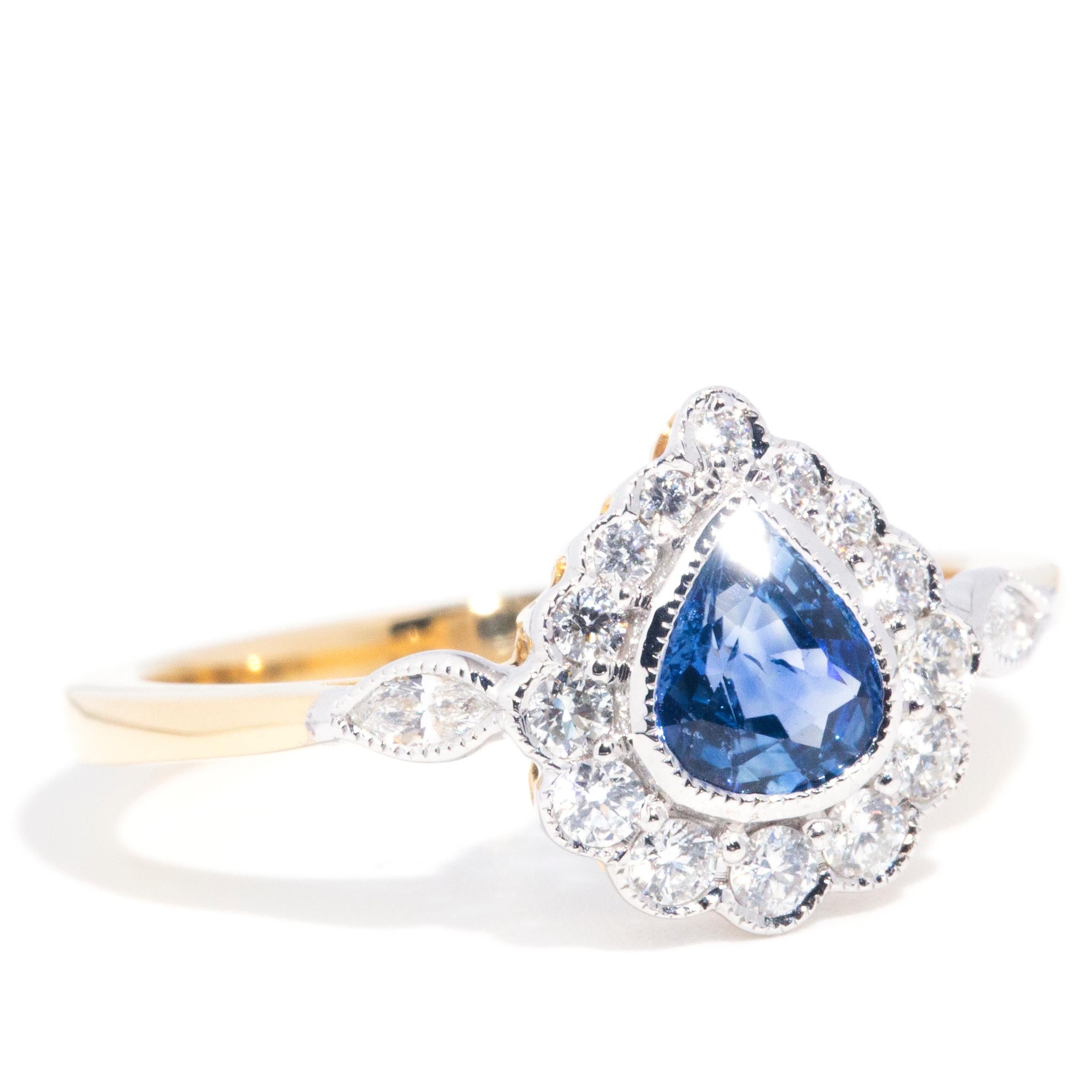 Lovingly crafted in 18 carat gold, this delightful halo ring features a gorgeous  bright blue pear cut blue sapphire resting in the centre and encompassed by a scintillating border of round brilliant diamonds. The graceful yellow gold band is