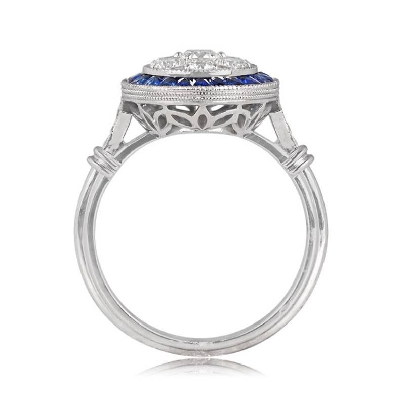 A captivating ring adorned with round brilliant cut diamonds, set within round bezels and held by prongs. These diamonds are encircled by a graceful halo of French-cut sapphires. Along the shoulders, more round brilliant cut diamonds twinkle,