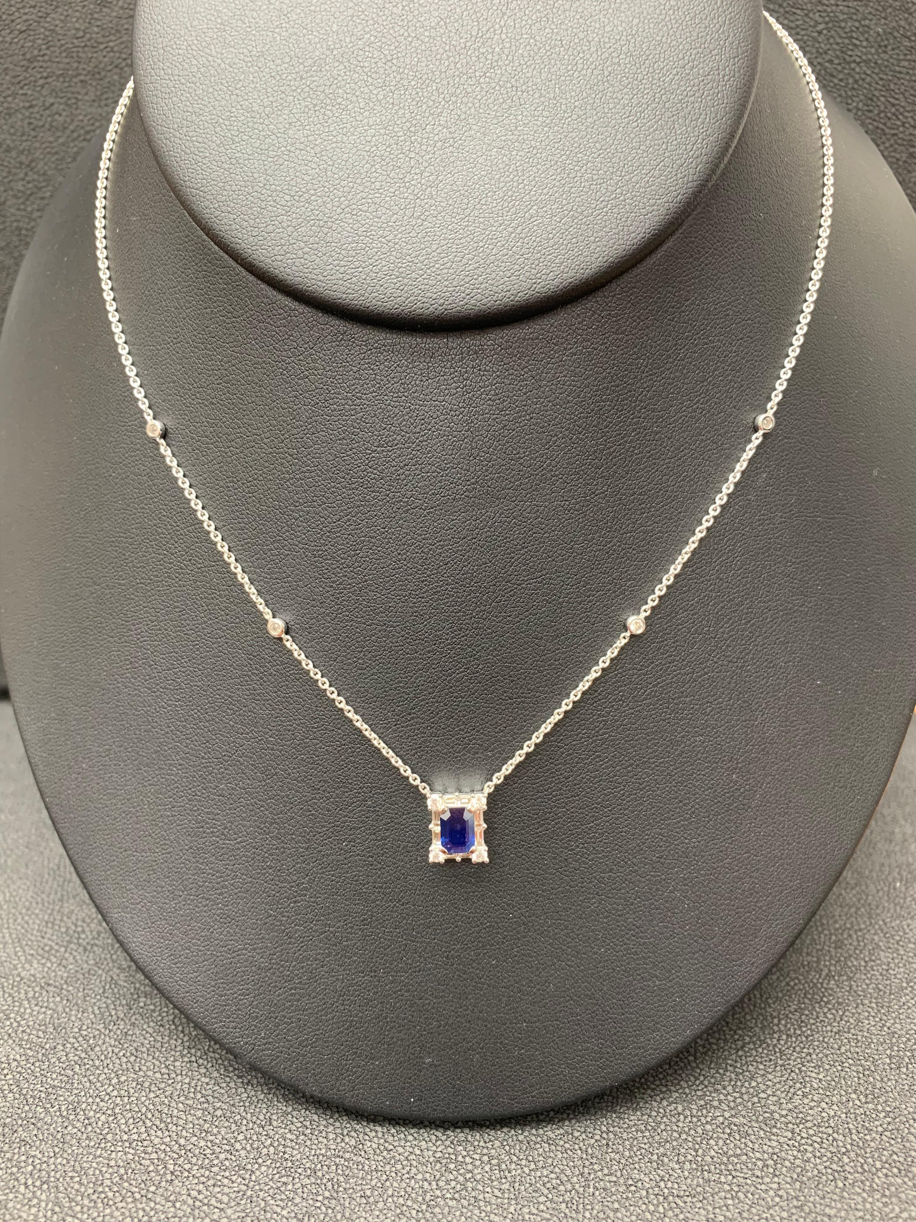 A fashionable pendant necklace showcasing a 0.72-carat emerald cut dark and vibrant blue color Sapphire. The center stone is surrounded by a row of brilliant-cut 8 round and 8 baguette diamonds weighing 0.58 carats total. Made in 18k white gold.