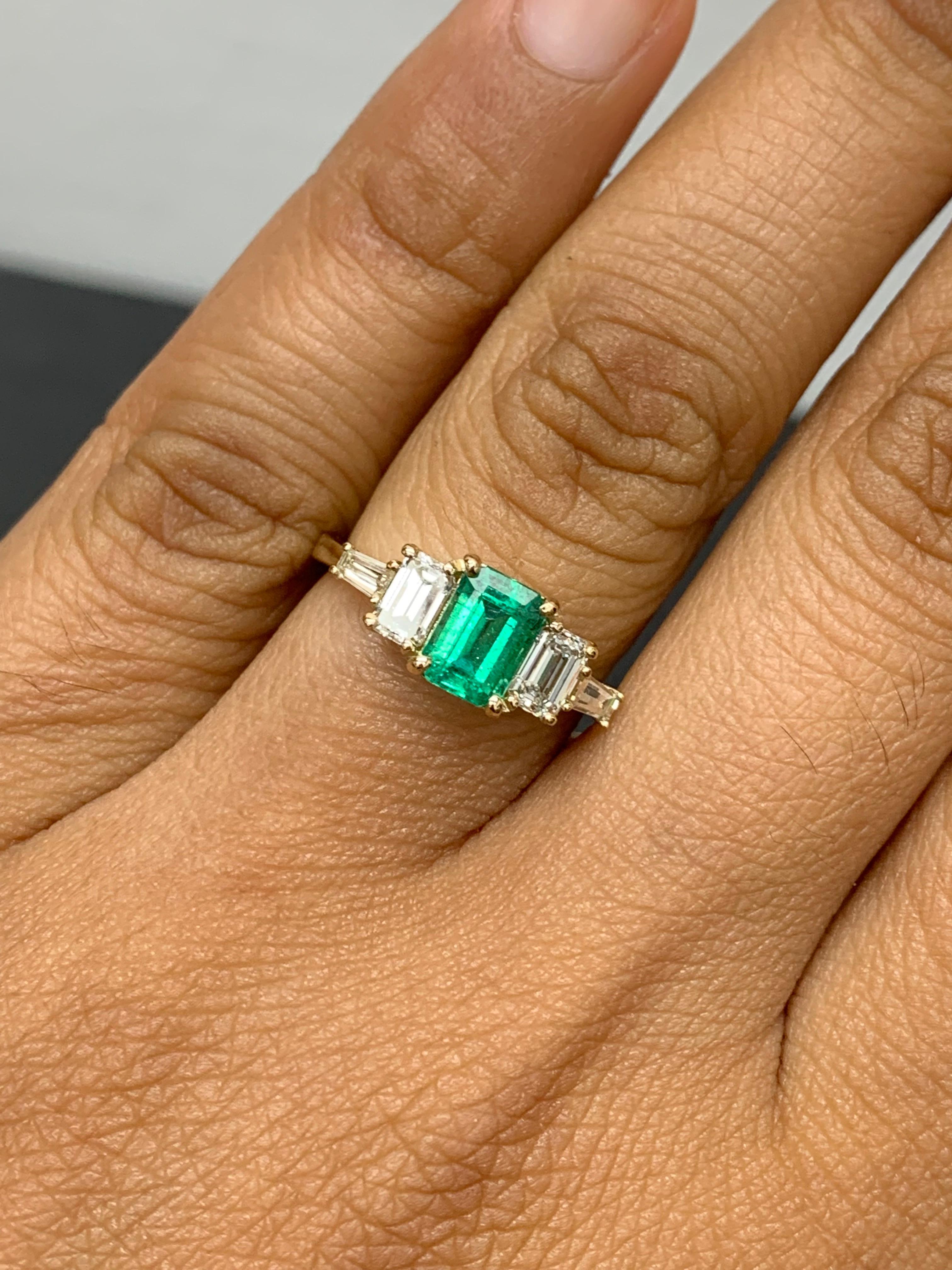Cette magnifique bague est ornée d'une riche émeraude d'un vert luxuriant intense pesant 0,72 carats.  La pierre centrale est flanquée de deux diamants de taille émeraude pesant 0,64 carat et de deux diamants baguette de chaque côté pesant 0,21