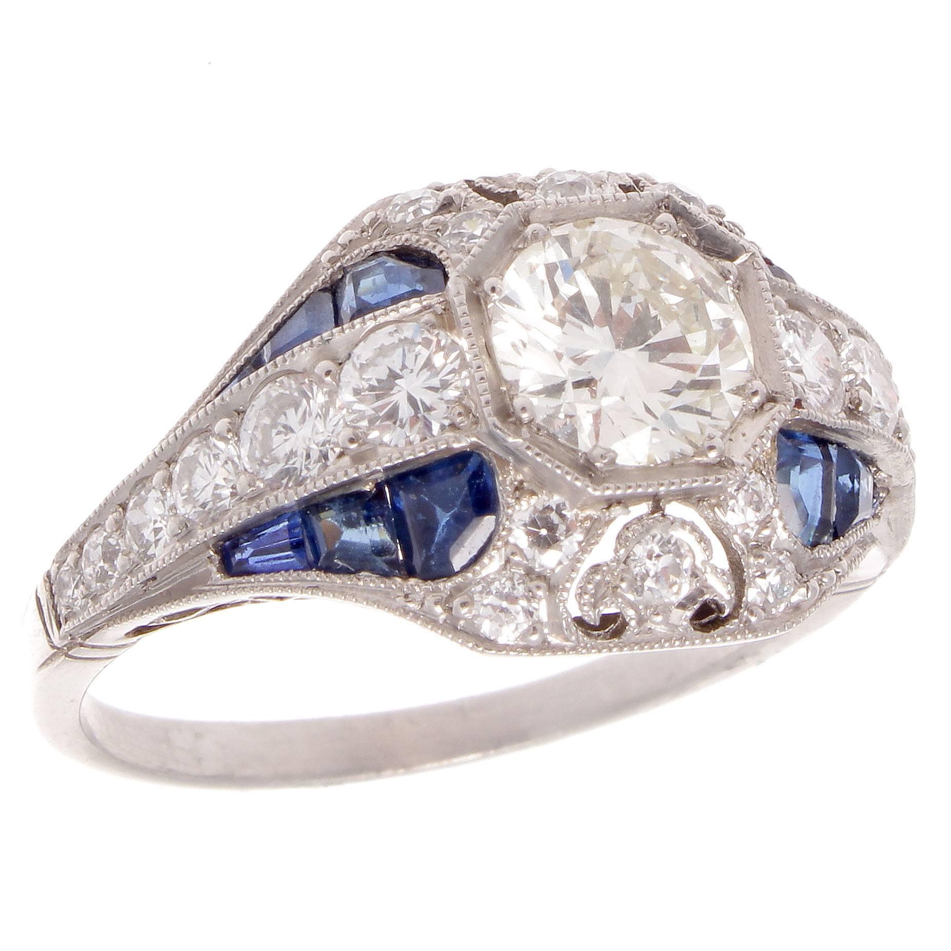Recreating the golden era of Art Deco jewelry with timeless designs of geometric elegance. Featuring a 0.72 carat round brilliant cut diamond that is I color, VS1 clarity. Perfectly framed by royal blue sapphires weighing approximately 0.60 carats