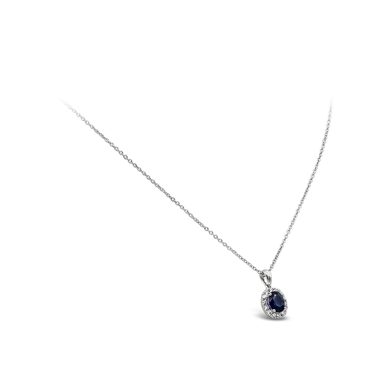 A classic pendant necklace, showcasing an oval cut blue sapphire weighing 0.73 carat, set on a four prong setting. Accented by a halo of round brilliant cut diamonds weighing 0.18 carat total. Finely made with 18K white gold. Suspended on a white