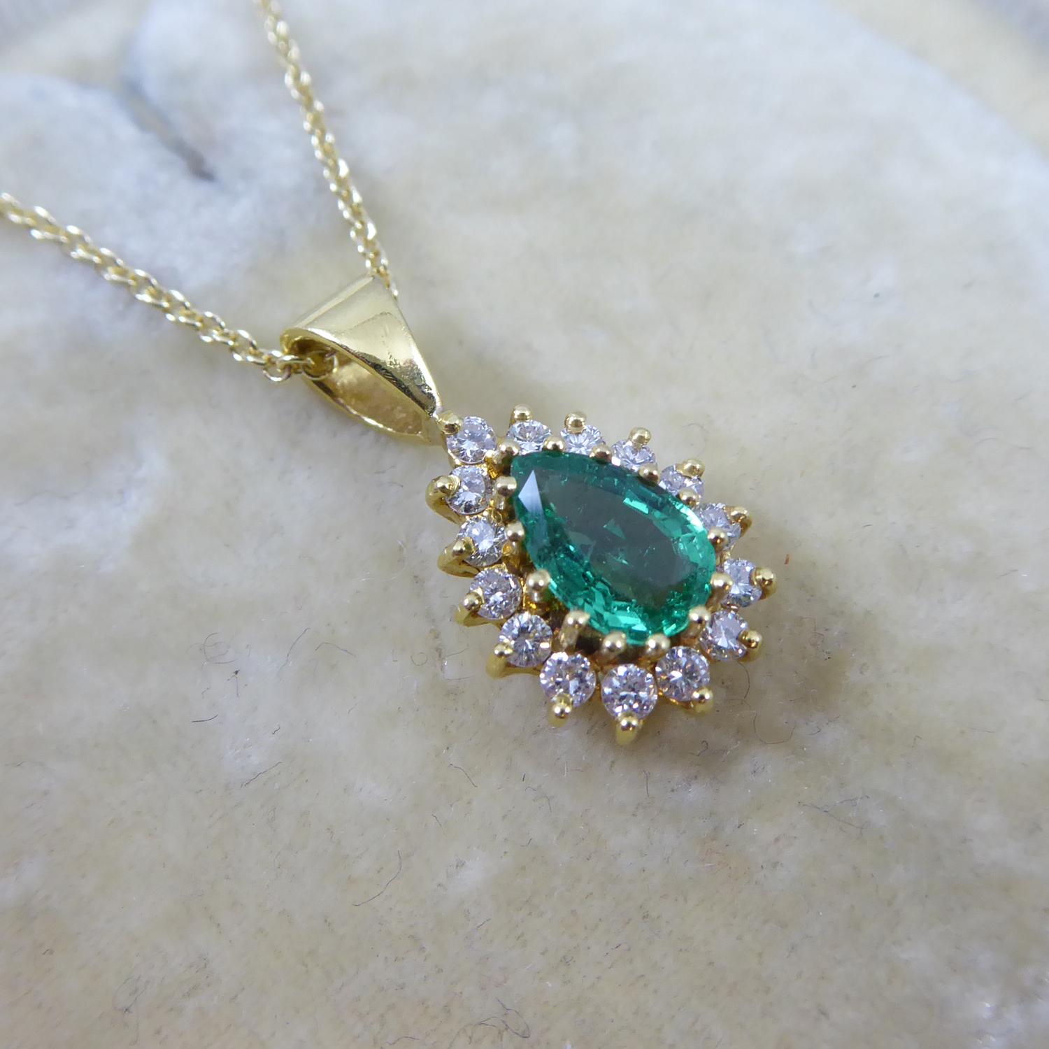 An emerald and diamond cluster pendant comprising a centrally set, pear-shaped, mixed-cut emerald of lightish green colour and strong saturation.  The emerald measures approx. 7.50mm x 5.10mm x 3.12mm.  A surround of 15 round, brilliant-cut