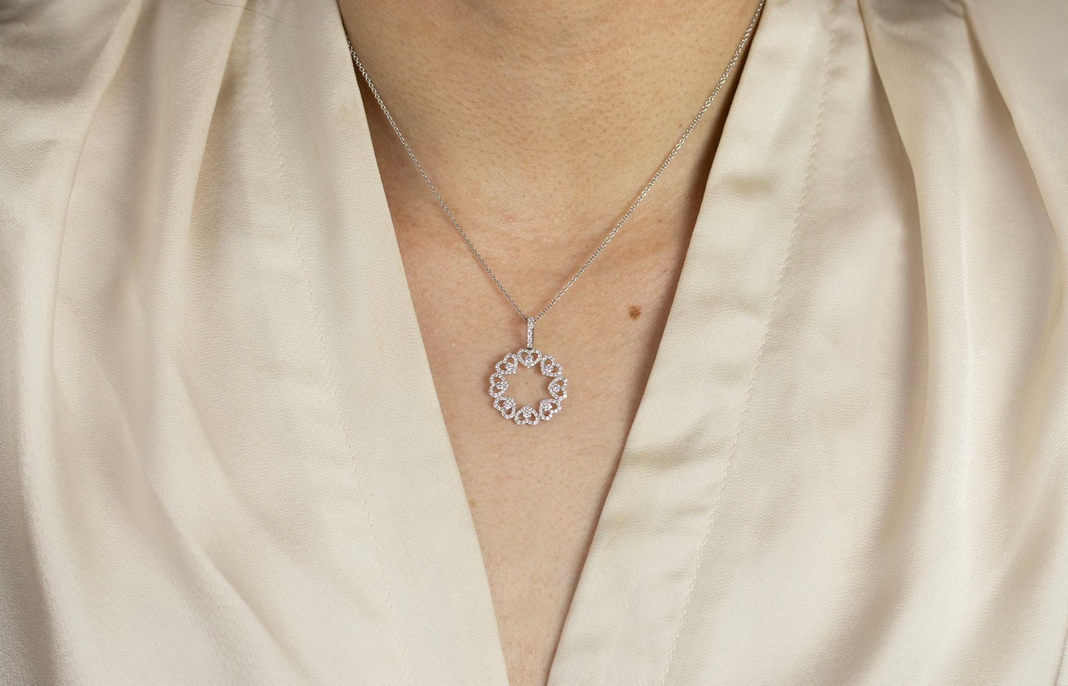 Un collier pendentif unique mettant en valeur des diamants ronds et brillants sertis en forme de petits cœurs autour d'un motif circulaire ajouré. Les diamants pèsent 0.73 carats au total. Fabriqué en or blanc 18 carats. Il est suspendu à une chaîne
