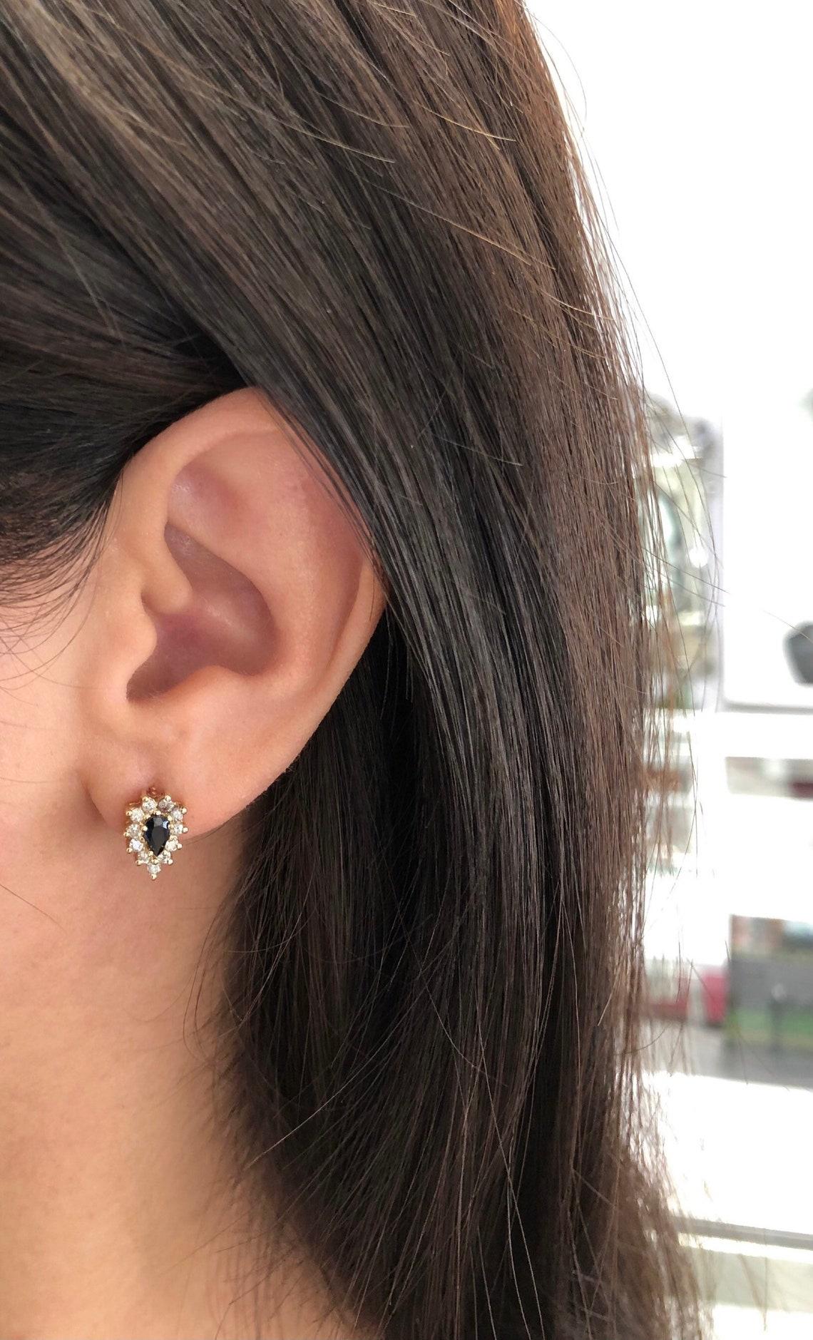 Featured here is a stunning set of pear-shaped blue sapphire & diamond halo stud earrings in fine 14K yellow gold. Displayed are deep, blue sapphires with incredible transparency, accented by a gorgeous diamond halo. The earth mined, sapphires have