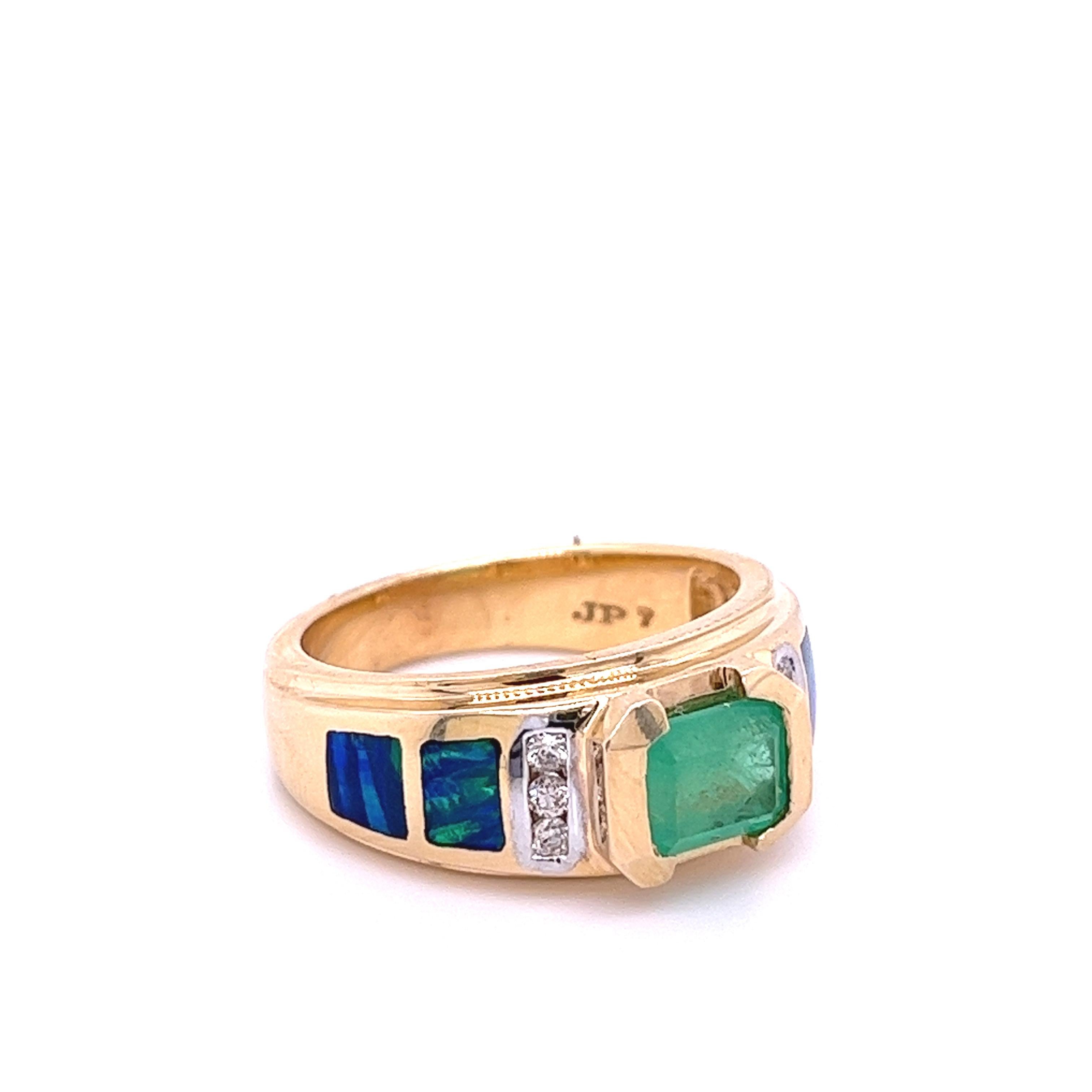 Sleek and classy Colombian Emerald ring with inlaid opals and diamond accents. Emerald-cut Emerald mounted in a 14k half bezel setting. Inlaid Opals provide excellent color contrast to the yellow gold setting and white diamond side stones. 

14k