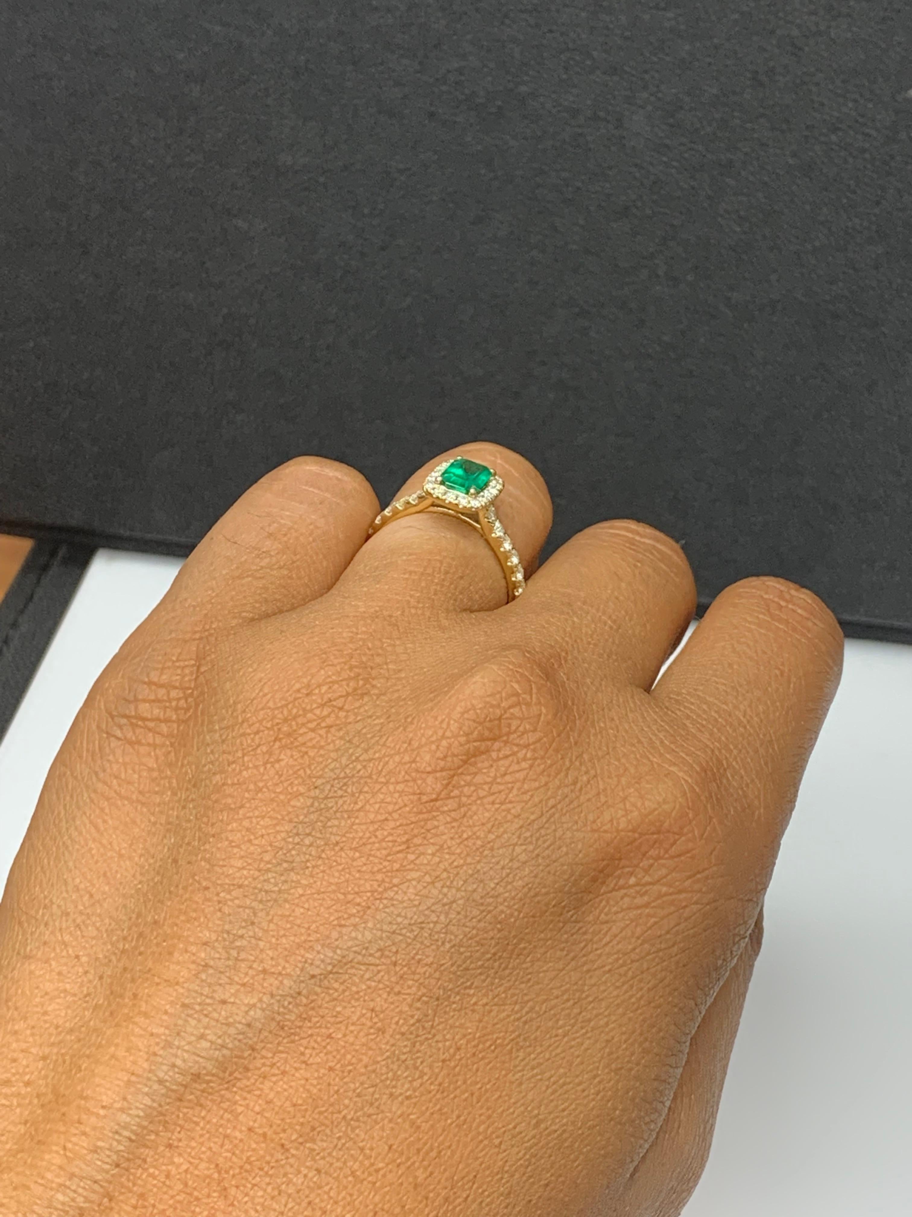 Présente une émeraude de taille émeraude pesant 0,77 carats, entourée d'une seule rangée de 30 diamants ronds de taille brillant dans un design de halo sans couture. Serti dans un fin anneau en or jaune 18 carats rehaussé de diamants. Les diamants