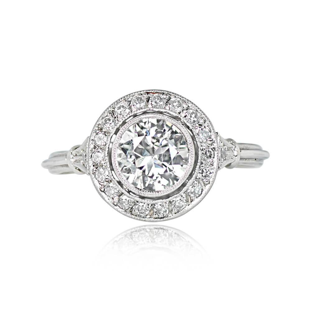 A vintage-style engagement ring features a bezel-set 0.79-carat old European cut diamond, J color, and SI2 clarity. The center stone is encircled by a halo of smaller old European cut diamonds. On each tapered shoulder, a single old European cut