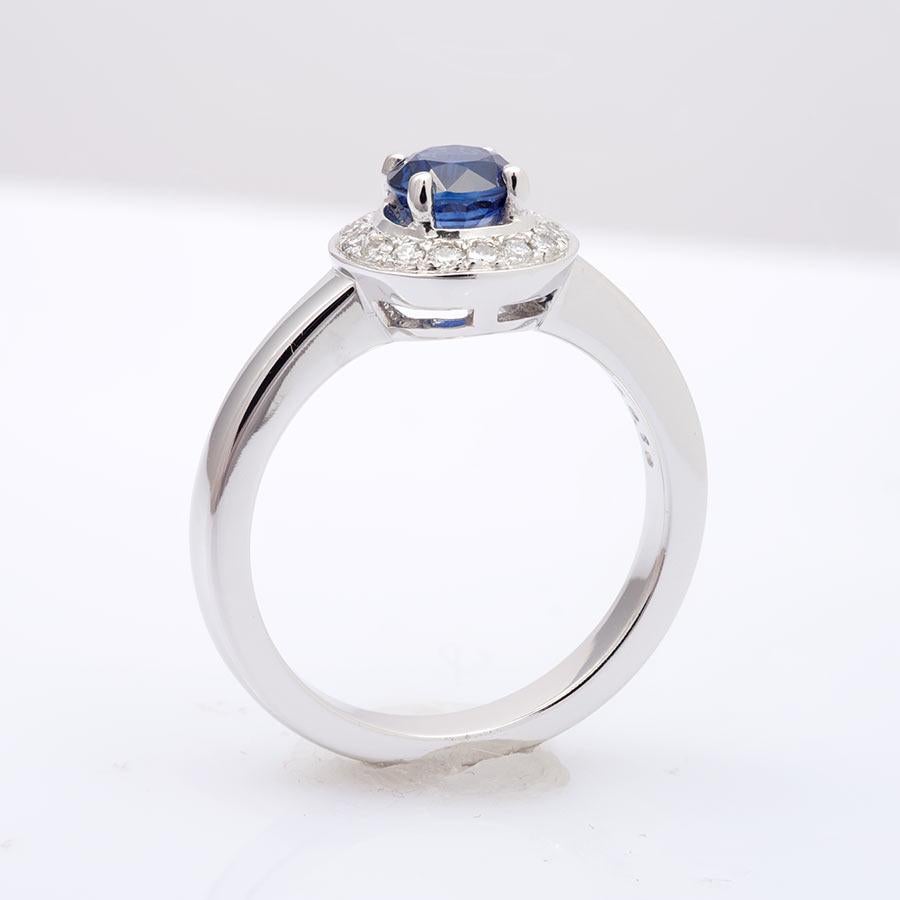 This stunning 14K white gold ring showcases a gorgeous blue Sapphire weighing 0.80 carats. Cut with great precision this gemstone displays no natural banding and has an even color tone. Around the center stone, the halo of diamonds brings just the