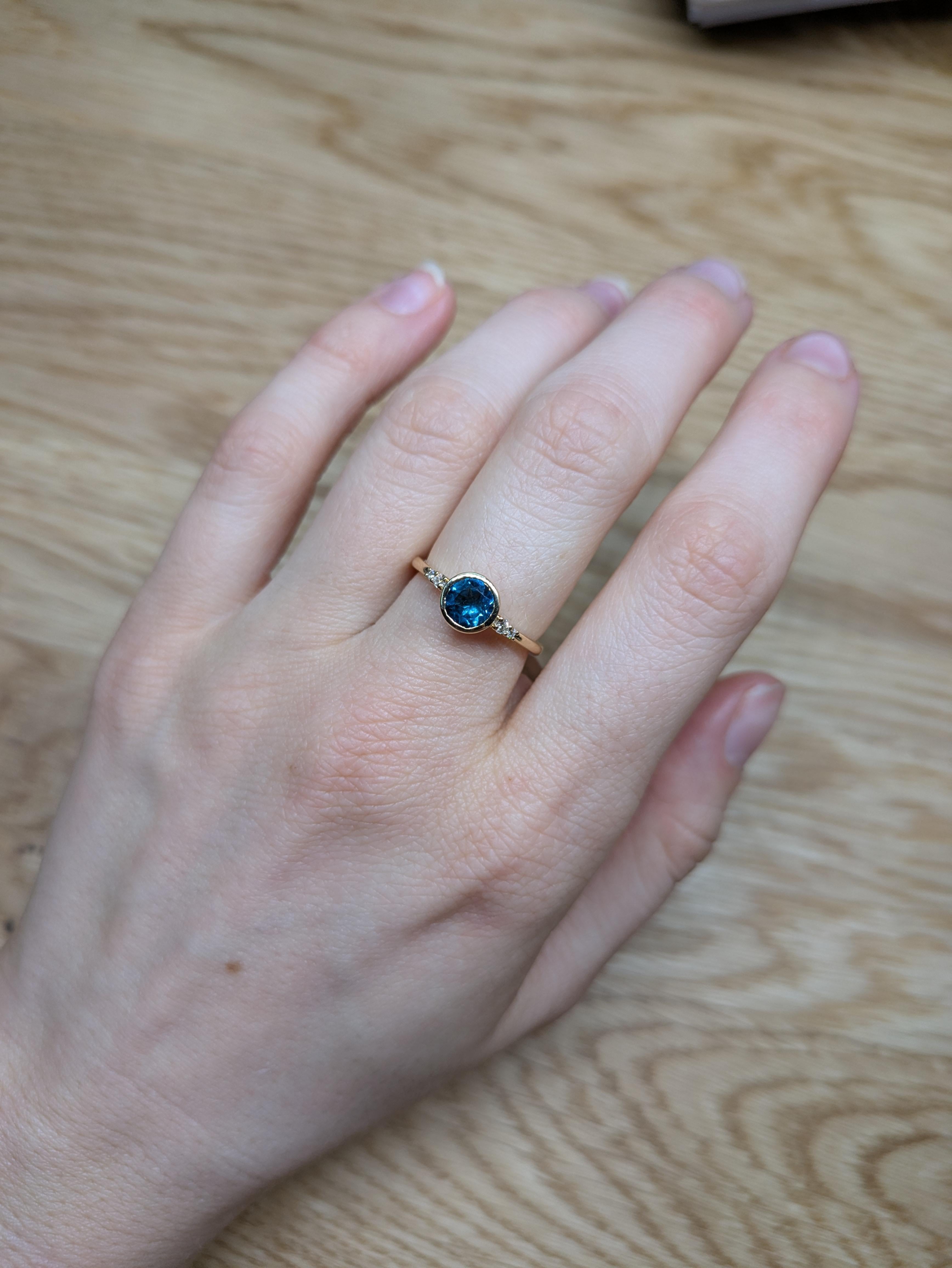 This ring is a breathtaking piece of jewelry that showcases the vibrant allure of a 0.80ct London Topaz set in luxurious 14K yellow gold. The gemstone, with its deep and captivating blue-green hue, is beautifully cut into a 6mm round shape, offering