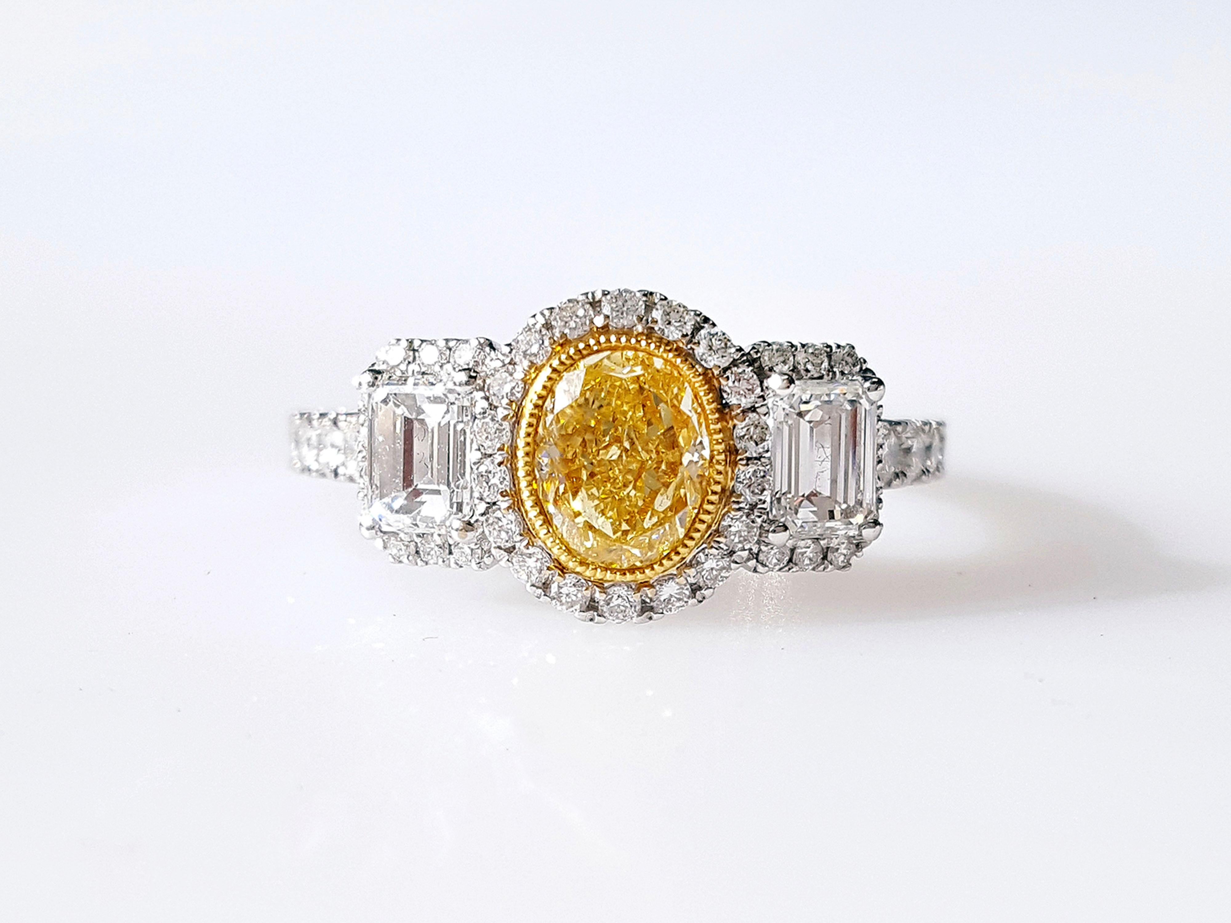 A stunning Three-Stones Engagement ring, 0.82 carat Yellow Oval-cut diamond. Flanked by two Emerald-cut diamonds total weight 0.58 carat. The classic design brings out the beauty of the center stone with the surrounding 46 round white diamonds 0.38