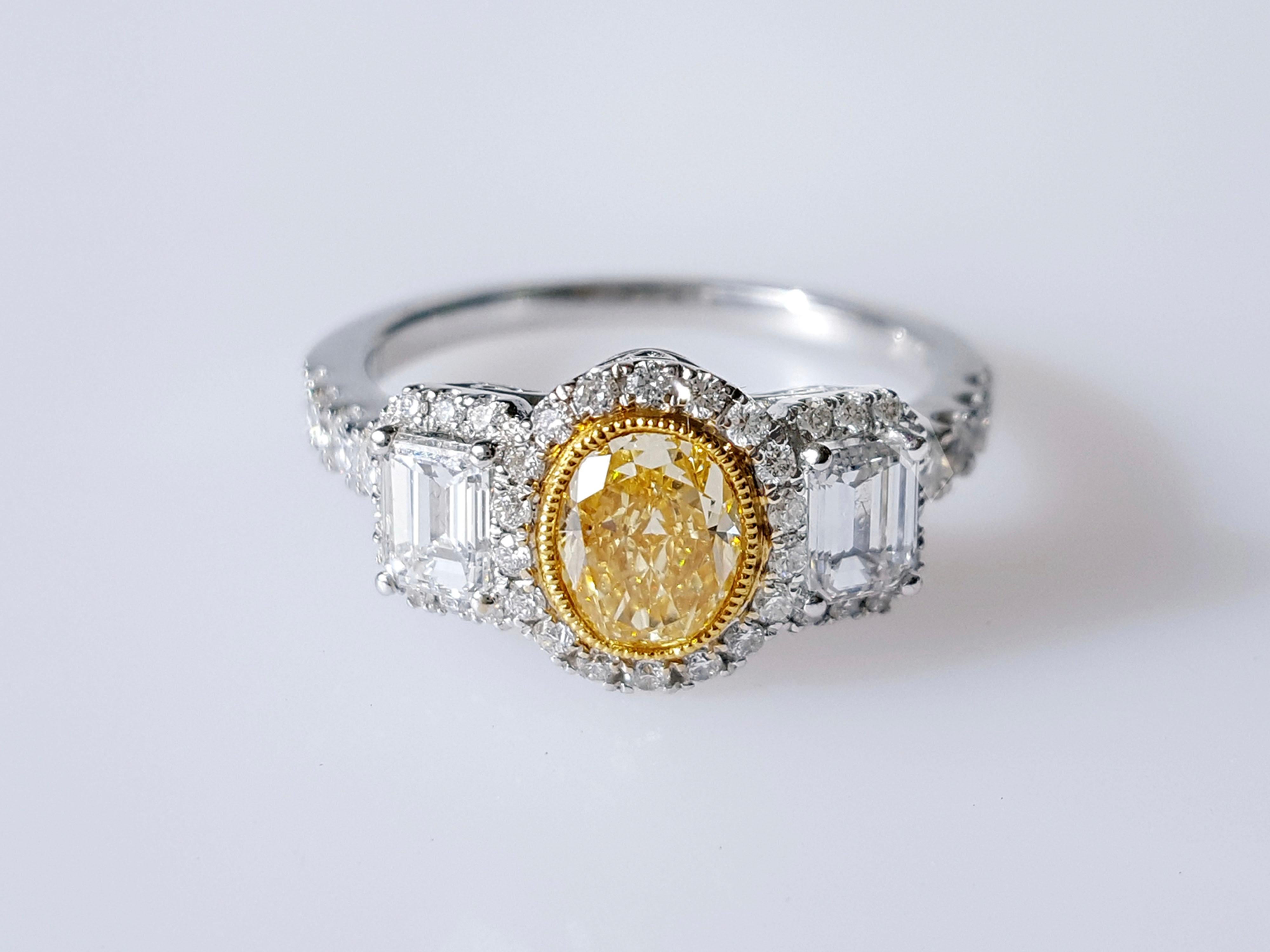 A stunning Three-Stones Engagement ring, 0.82 carat Yellow Oval-cut diamond. Flanked by two Emerald-cut diamonds total weight 0.58 carat. The classic design brings out the beauty of the center stone with the surrounding 46 round white diamonds 0.38
