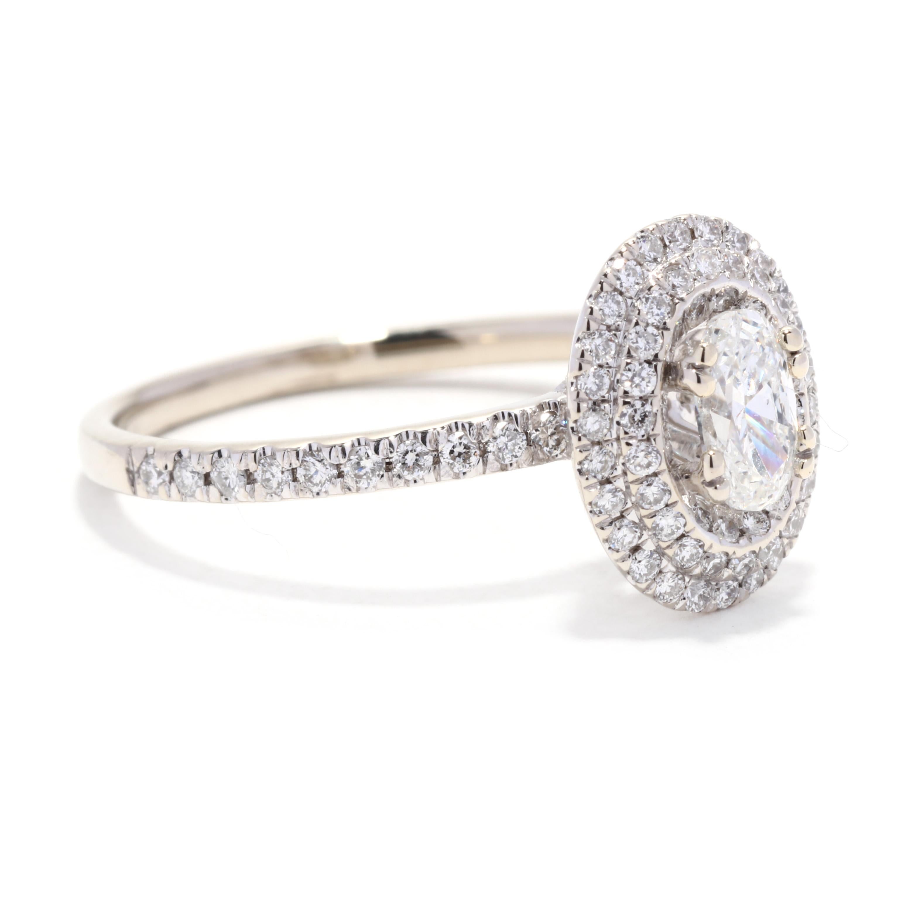 A 14 karat white gold oval diamond halo engagement ring. This simple engagement ring features a prong set, oval cut diamond weighing approximately .32 carat surrounded by a double halo of pavé set diamonds and down the band weighing approximately