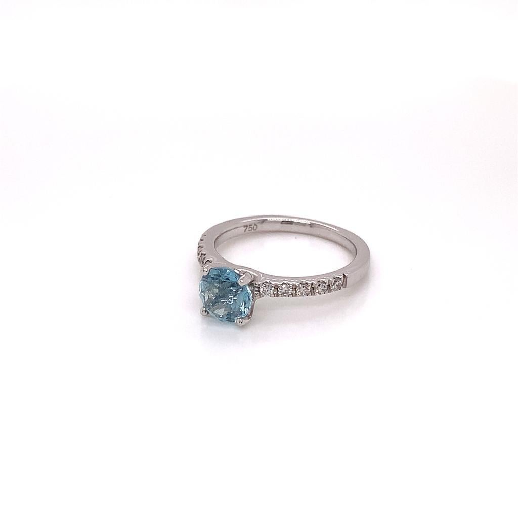 Cette élégante bague présente en son centre une aigue-marine de forme ronde et brillante pesant environ 0,84 carat, ainsi qu'une rangée de diamants de forme ronde et brillante sur l'anneau en or blanc 18 carats. L'aigue-marine est une belle nuance