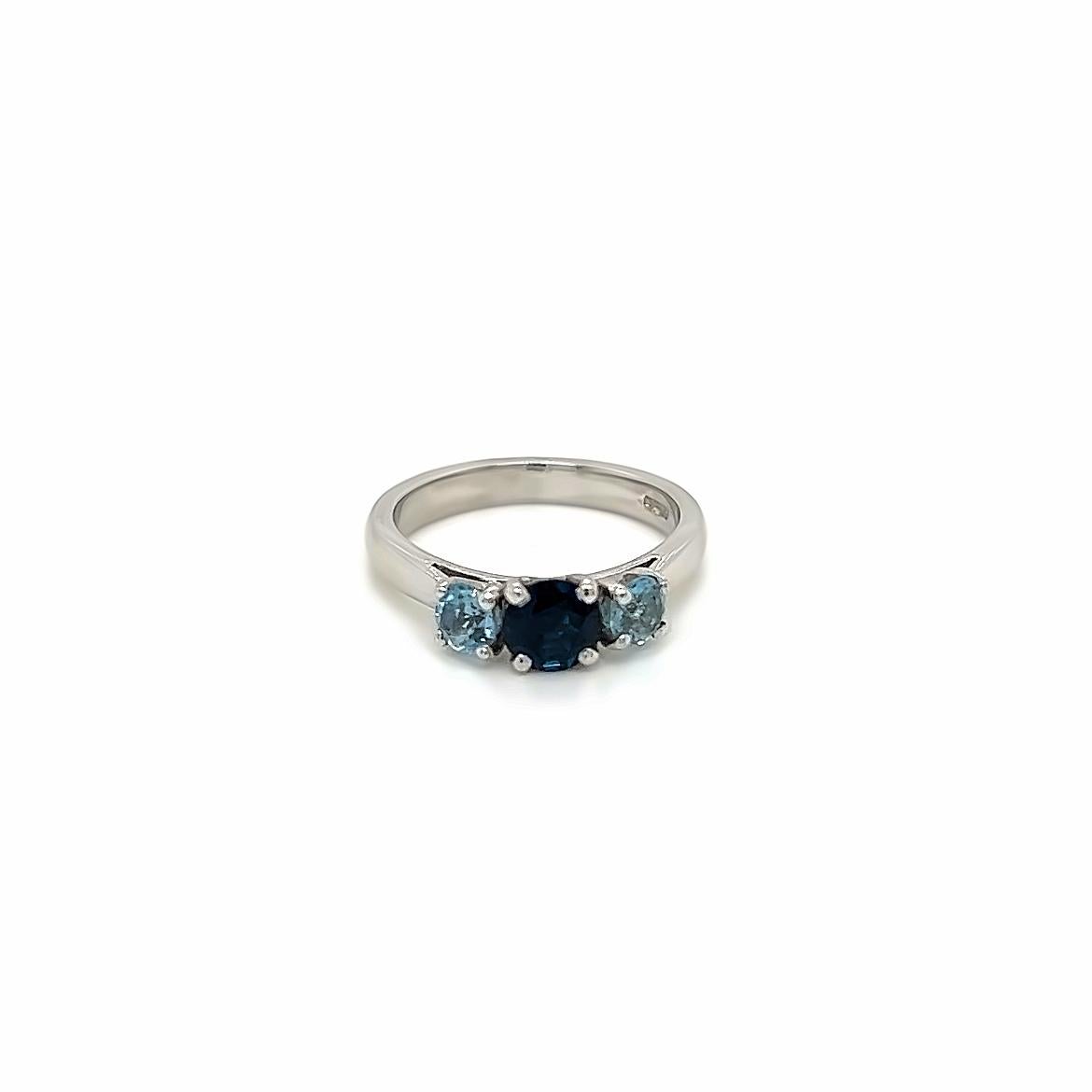 This gorgeous three-stone ring features a Round Brilliant Blue Sapphire at its centre, with smaller round brilliant aquamarines on either side of it. The precious stones are held in a claw setting on a Platinum band.

The luscious blue sapphire