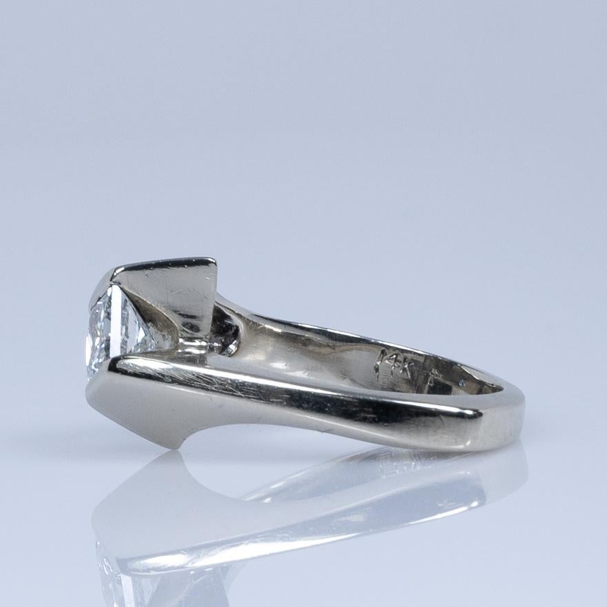 This elegant engagement ring features a Euro shank design and a semi bezel-set princess cut diamond, crafted from 14k white gold. The unique setting beautifully highlights the diamond, offering both security and a modern aesthetic. A perfect blend