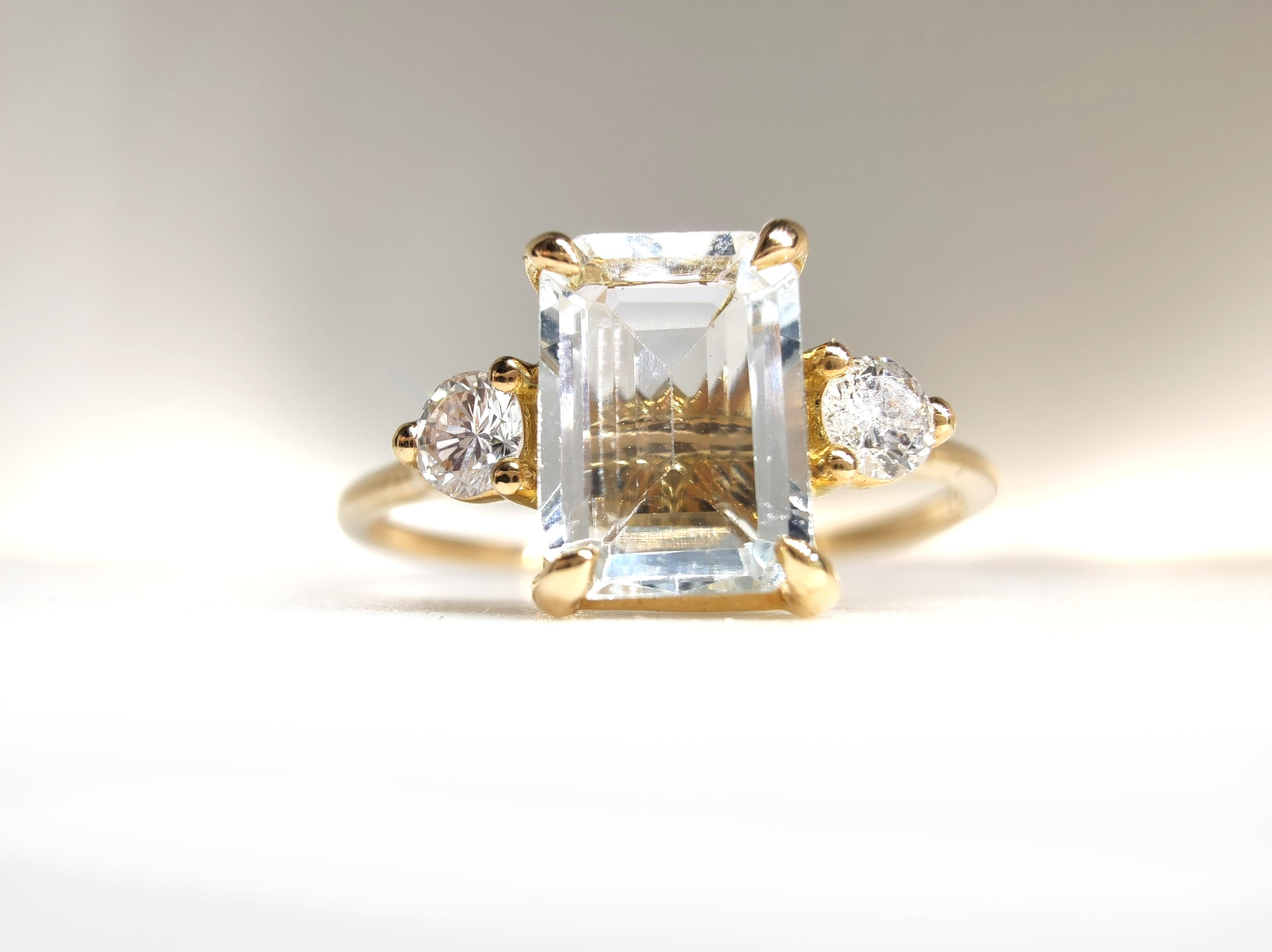 Célébrez l'élégance et la signification avec cette bague à trois pierres fabriquée à la main, méticuleusement sertie dans de l'or jaune massif 18K. Cette pièce raffinée présente en son centre une aigue-marine naturelle de 0,88 carat taillée en