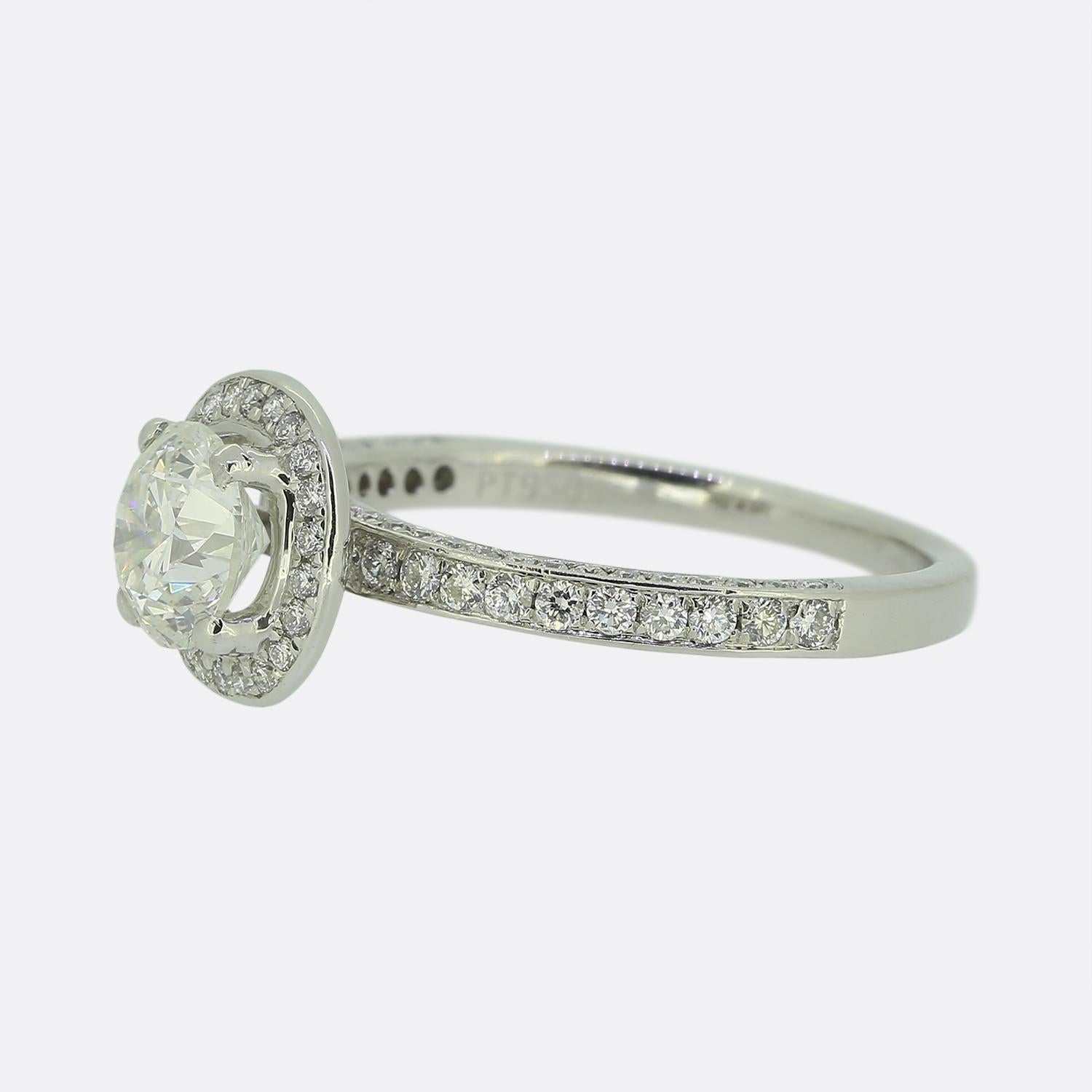 Aquí tenemos un anillo de compromiso clásico con halo de diamantes. Esta pieza contemporánea se ha elaborado en platino y lleva un diamante redondo de talla brillante de 0,90 quilates en el centro de la cara. Esta piedra principal está engastada en