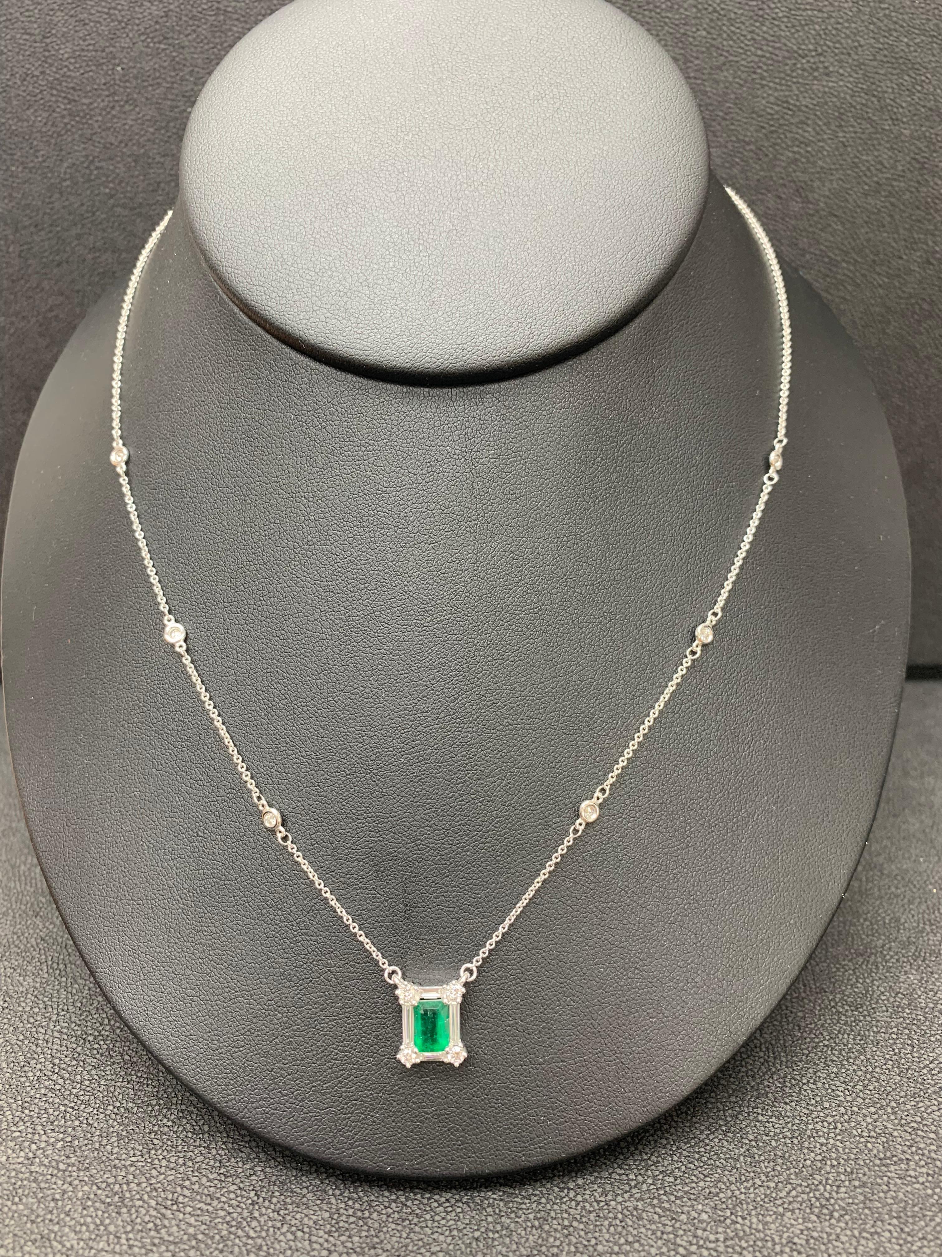 A fashionable pendant necklace showcasing a 0.90 carat emerald cut lush green emerald. The center stone is surrounded by a row of brilliant-cut round and baguette diamonds weighing 0.63 carats total. Made in 14k white gold. Comes with a gold chain