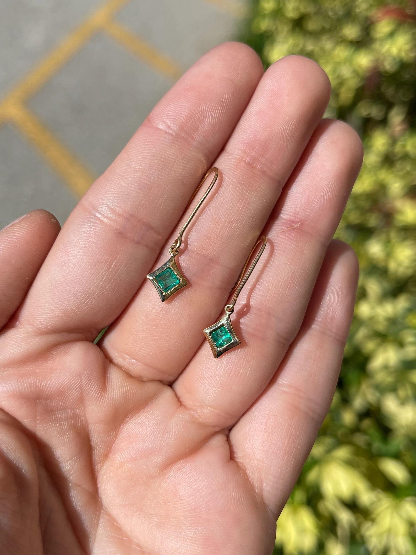 A stylish and modern pair of solitaire emerald dangle earrings. This dainty pair showcases two remarkable Asscher cut Colombian emeralds, bezel set within a solid 14K yellow gold dangles.

Setting Style: Bezel
Setting Material: 14K Yellow