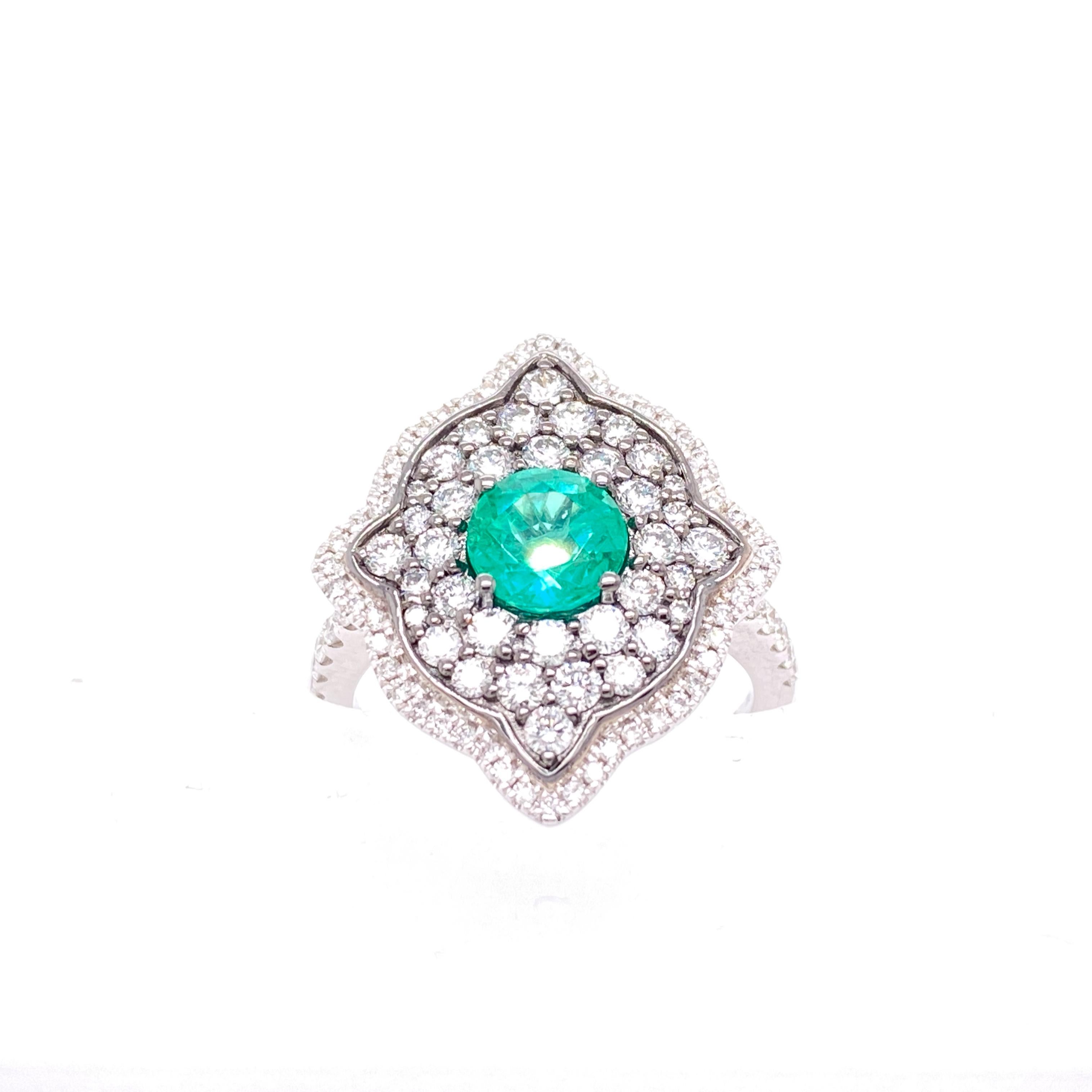 This stunning Cocktail Ring features a beautiful 0.91 Carat Round Emerald surrounded by Radiant Round White Diamonds, that sits on a Diamond Shank. This Ring is set in 18K White Gold. Total Diamond Weight = 0.99 carats. Ring Size is 6 1/2.