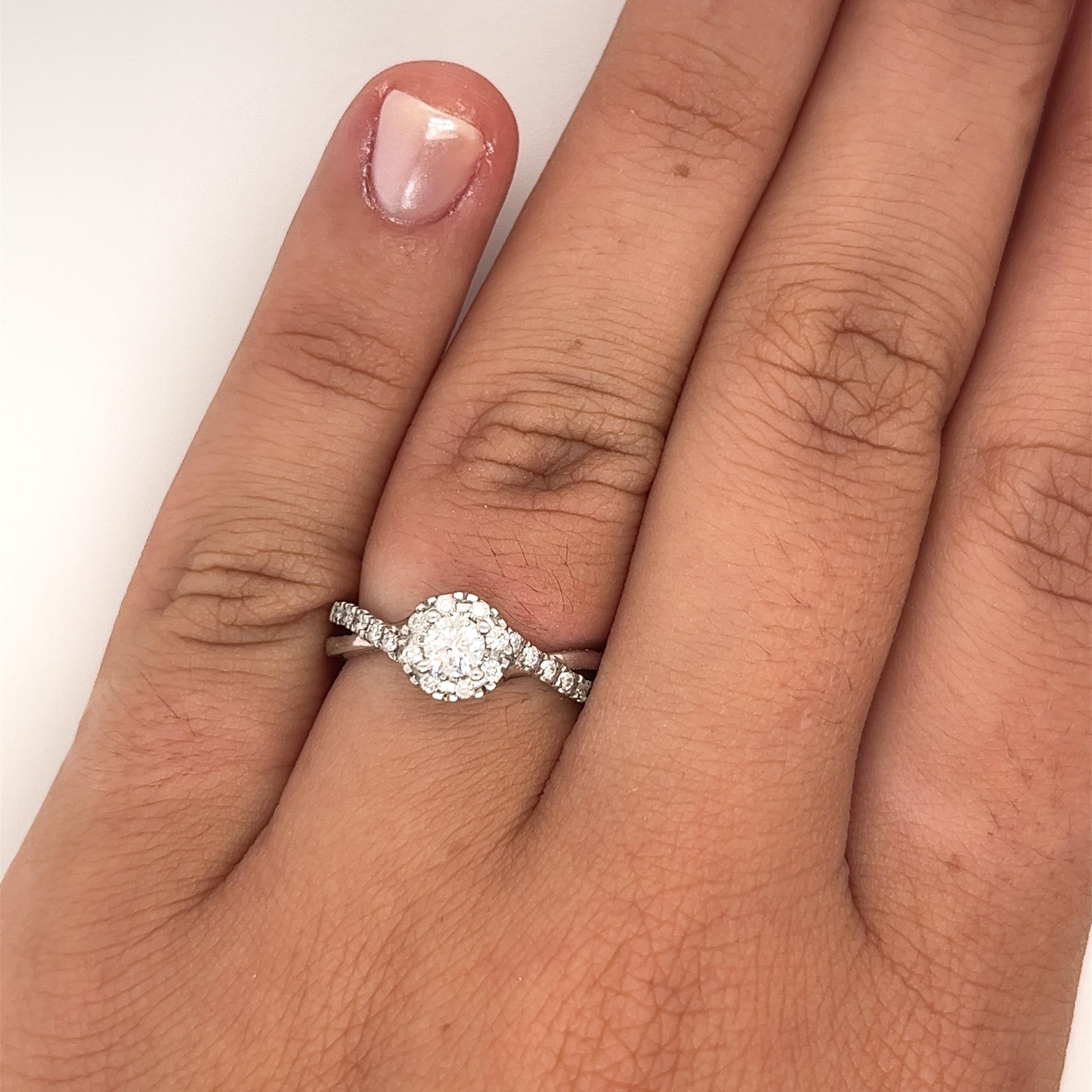 10K white gold natural diamond engagement ring. Featuring a 0.25 carat round cut diamond center stone, with G color and SI2 clarity. Adorned with a diamond halo and diamond side stones with a total 0.66-carat weight. All securely held with prong