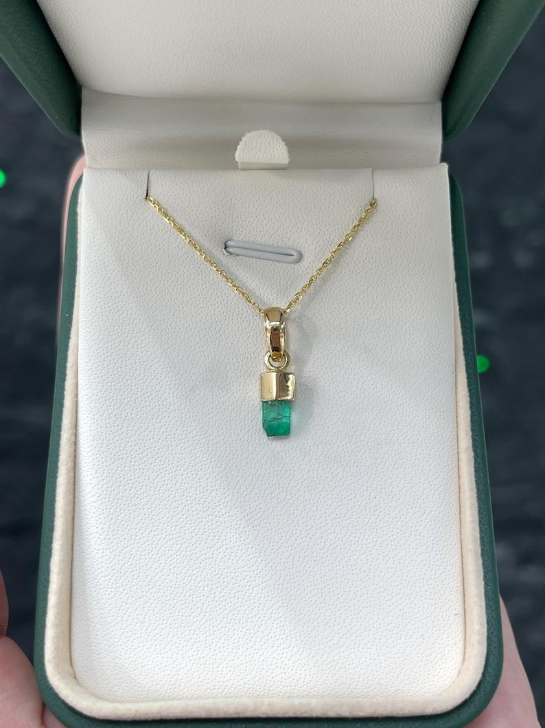 Ti presentiamo il nostro ciondolo di smeraldo grezzo naturale: un sorprendente cristallo di smeraldo colombiano da 0,92 carati che passa da un verde intenso nella parte inferiore a un verde medio nella parte superiore. Incastonato in un radioso oro