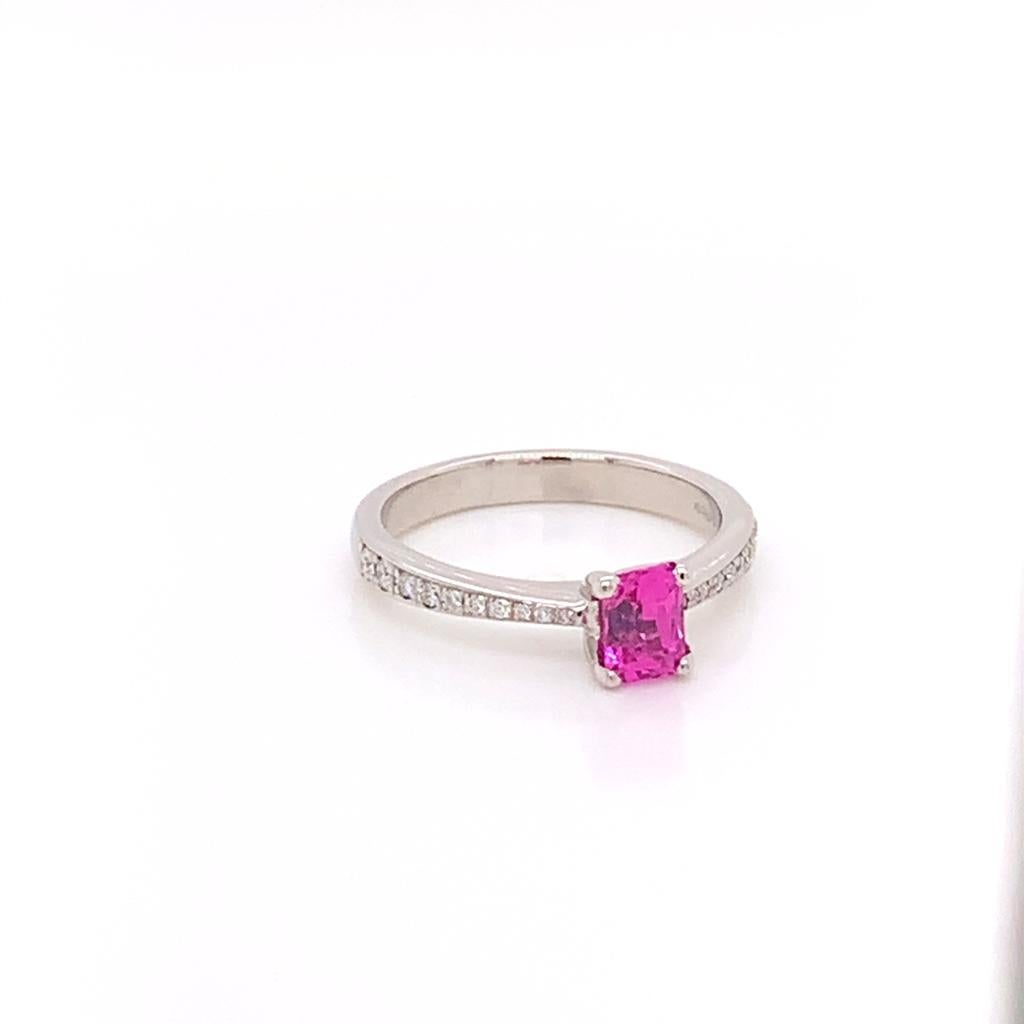 This stylish ring features a Cushion cut Pink Sapphire held in a claw setting on a Platinum Band, with Round Brilliant shoulder Diamonds on either side of it. The pink sapphire weighs 0.94 Carats, and the diamonds accompanying it weigh a total of