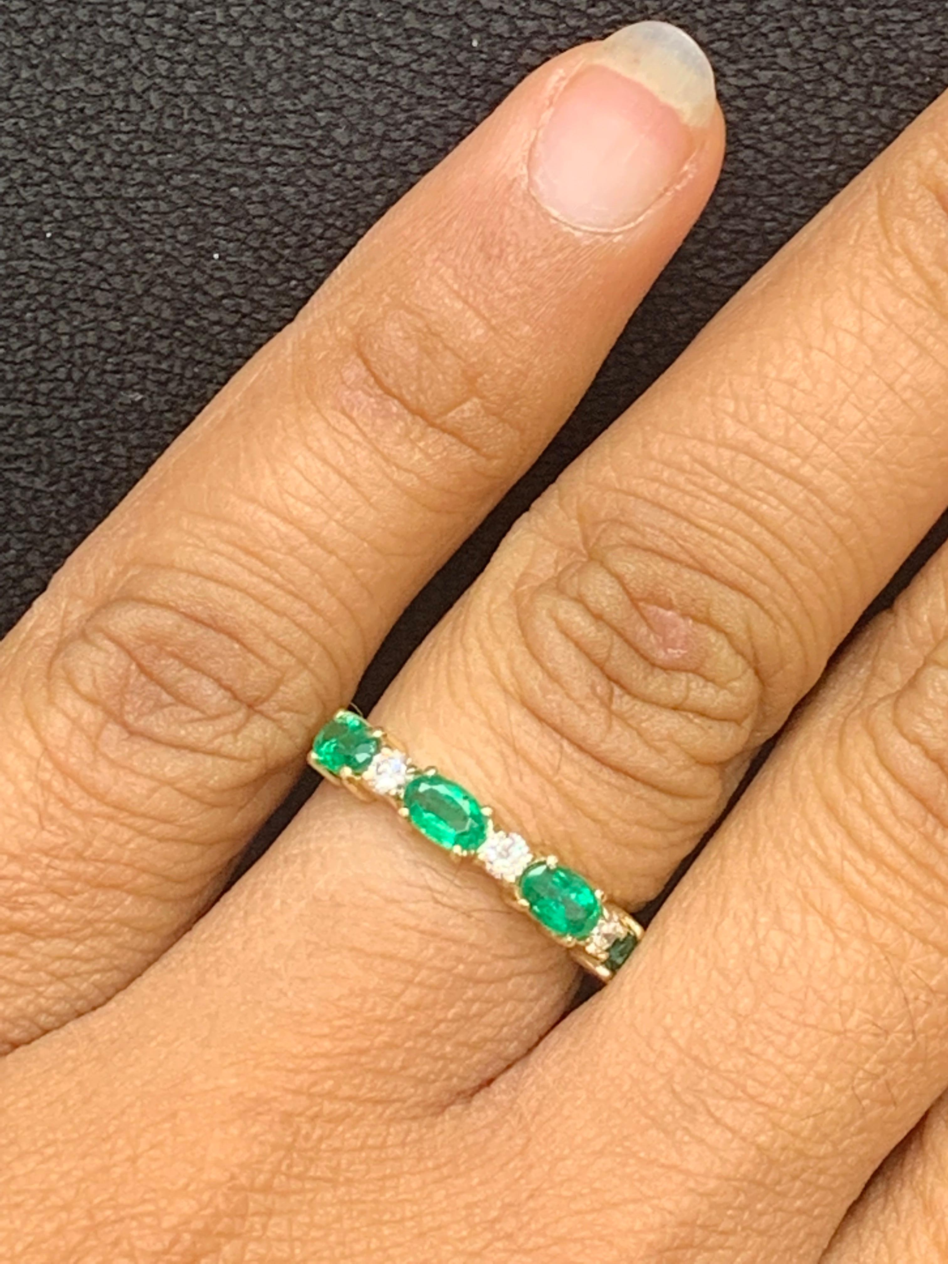 A unique and fashionable wedding band style showcasing 5 Oval Cut Emerald spaced by brilliant-cut diamonds, set in a shared-prong open gallery mounting made in 14k yellow gold. Emeralds weigh 0.94 carats total; diamonds weigh 0.20 carats total. Size