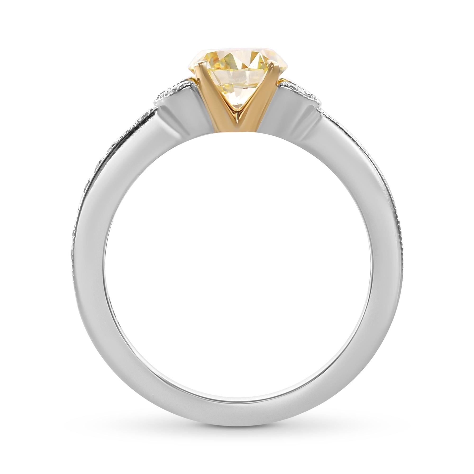 Questo elegante anello di fidanzamento presenta un diamante rotondo giallo fantasia da 0,94 carati con purezza VVS2, certificato da GIA. Incastonato in un mix di oro bianco e giallo 18 carati, mostra intricati disegni di foglie in pavé lungo il