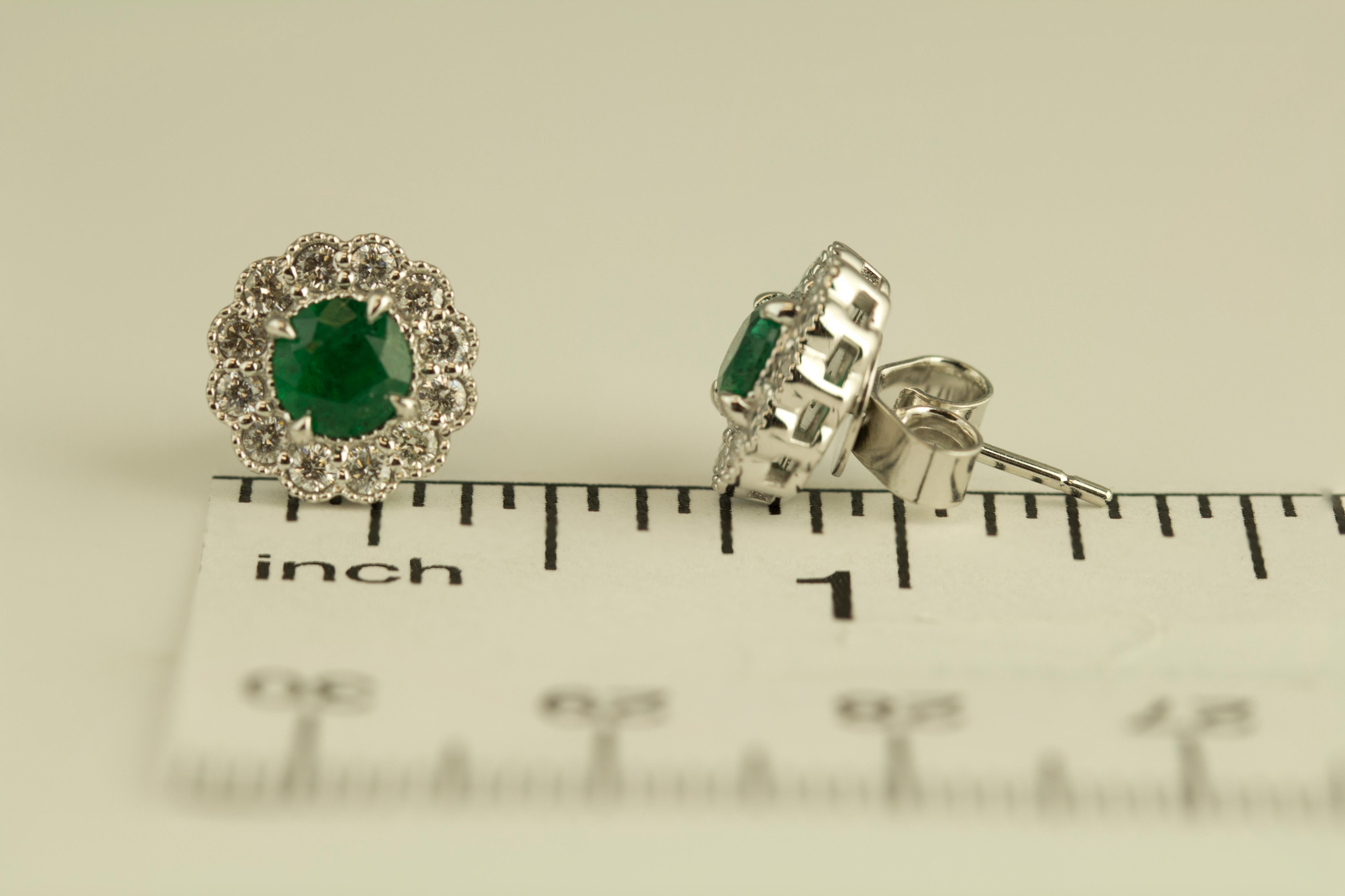 Presenting these stunning earrings showcasing two round-cut emerald centers, enveloped by a halo of round natural diamonds. Delicate milgrain detailing throughout the design enhances its overall floral aesthetic. The total emerald weight is 0.95