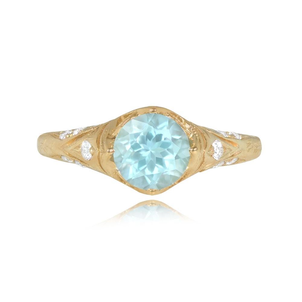 This ring showcases a 0.96-carat round aquamarine held in prongs. The 18k yellow gold openwork setting is adorned with round brilliant cut diamonds totaling around 0.14 carats. The mounting is intricately detailed with hand engravings along the