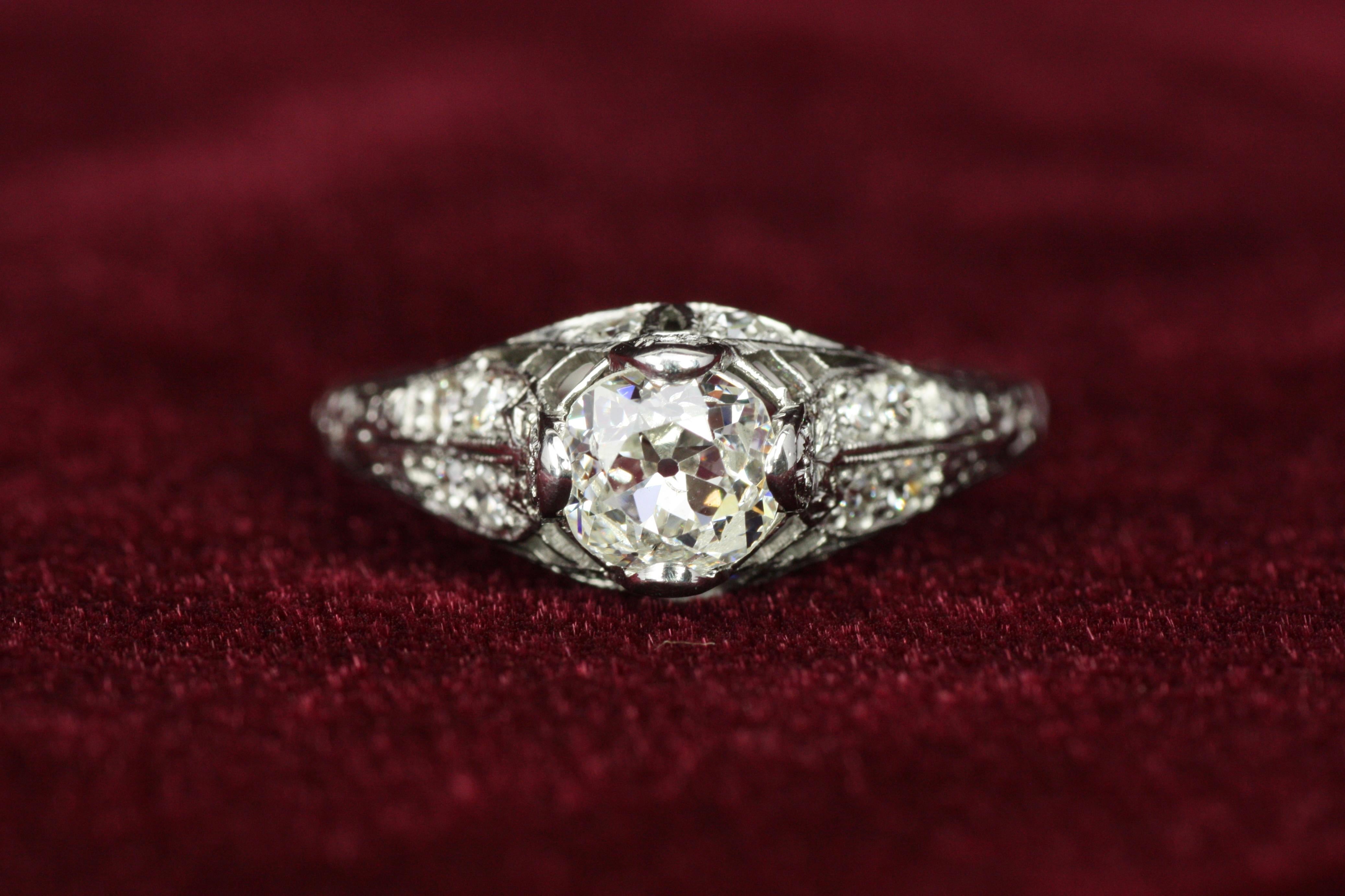 Questo squisito anello di fidanzamento in platino Art Deco degli anni '20 presenta un diamante centrale da 0,68 carati con taglio Old Mine, splendidamente completato da diamanti rotondi a taglio singolo lungo i lati. Il suo design in filigrana
