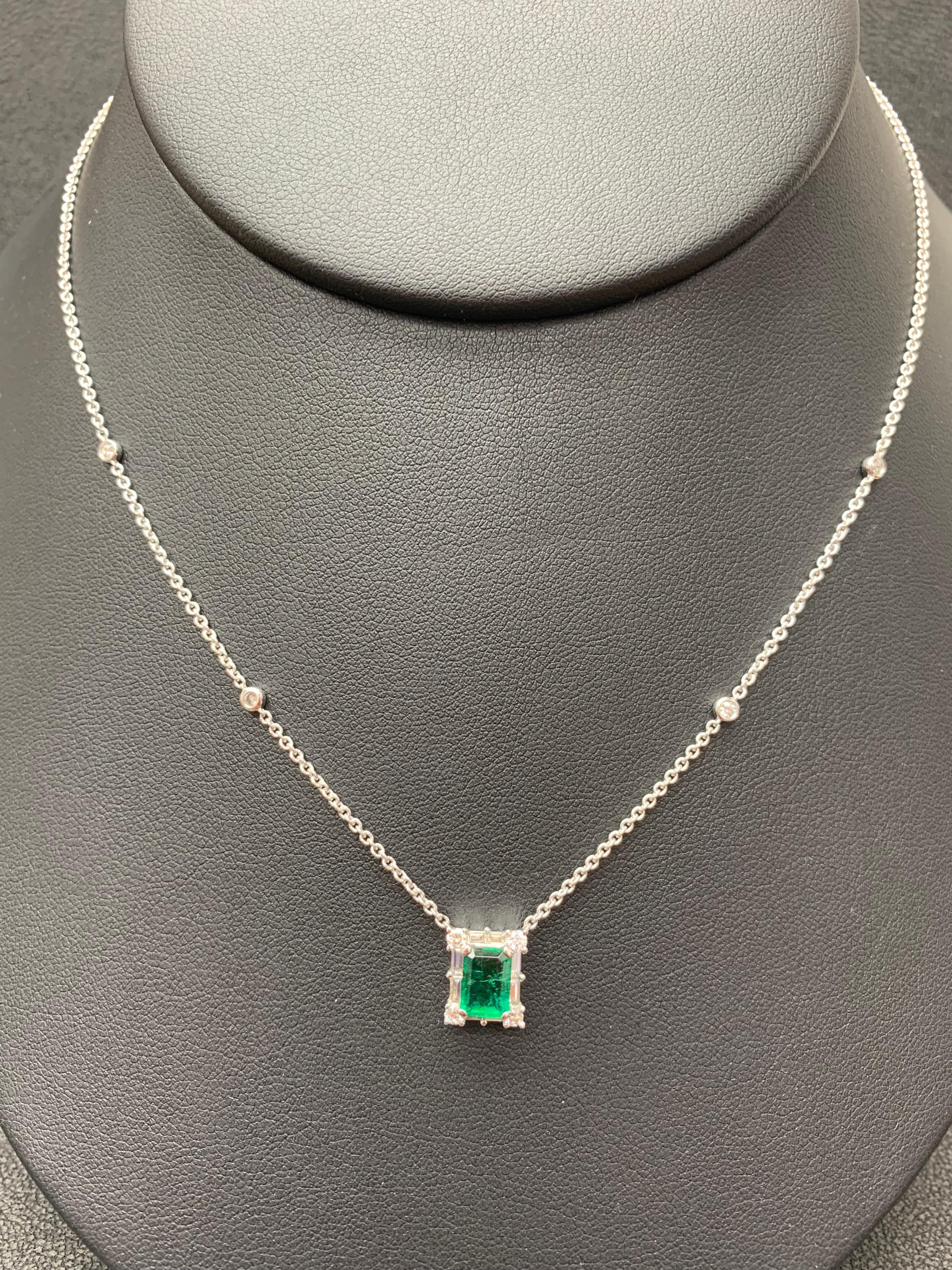 A fashionable pendant necklace showcasing a 0.99-carat emerald cut lush green emerald. The center stone is surrounded by a row of brilliant-cut 8 round and 8 baguette diamonds weighing 0.58 carats total. Made in 18k white gold. Comes with a gold