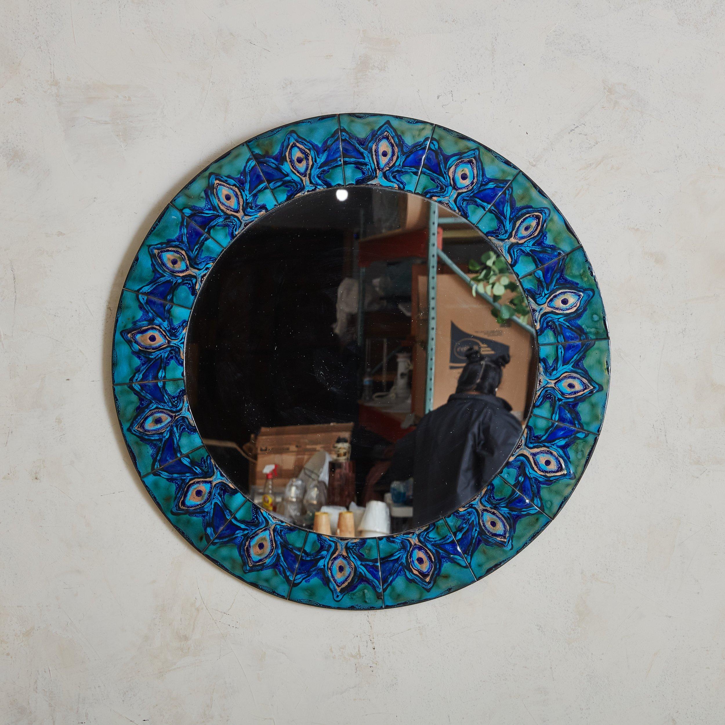 A Scandinavian Modern round wall mirror by Bodil Hagedorn Eje. Daughter of painter Thorvald Hagedorn-Olse, Bodil Eje was a Danish artist from the 20th Century who mostly worked with enamel. The mirror’s frame is composed of enameled copper plates