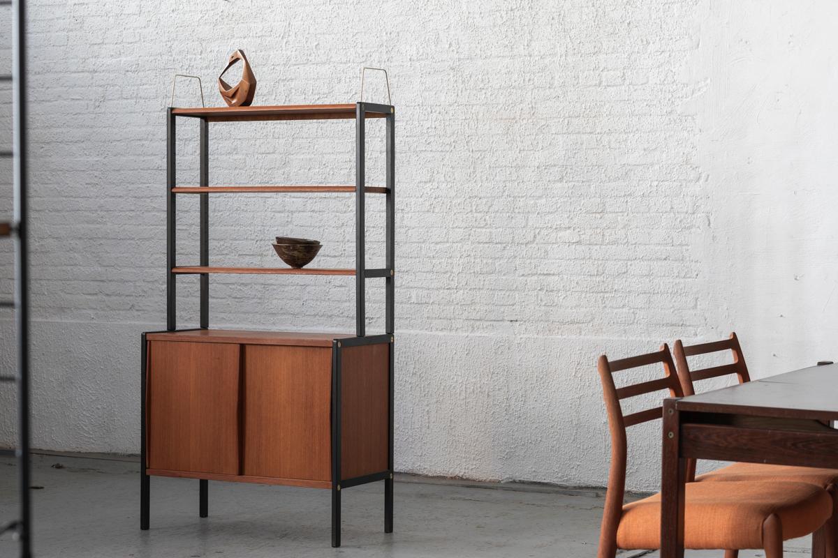 Freestanding shelving system by Bertil Fridhagen, designed and produced in Sweden in the 1960’s. Standing metal supports combined with teak wooden elements. The system features one sliding door cabinet and three shelves. The top part can be easily