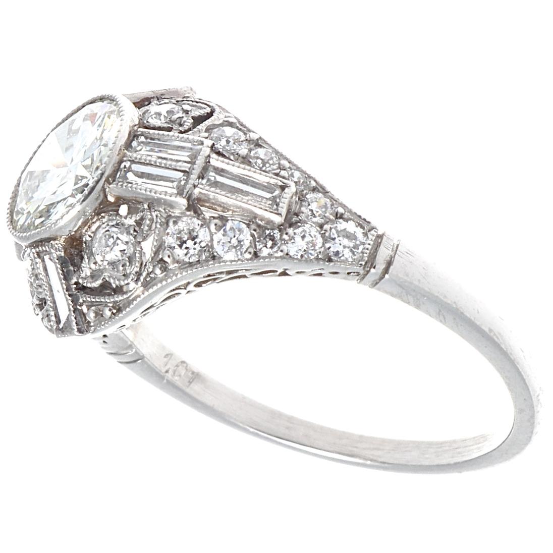 Everything you want in a platinum engagement ring. A beautiful 1 carat round brilliant diamond with accenting baguette cut diamonds and filigree design conspire to create a stunning ring with a shimmering presence. There are 8 baguette cut diamonds