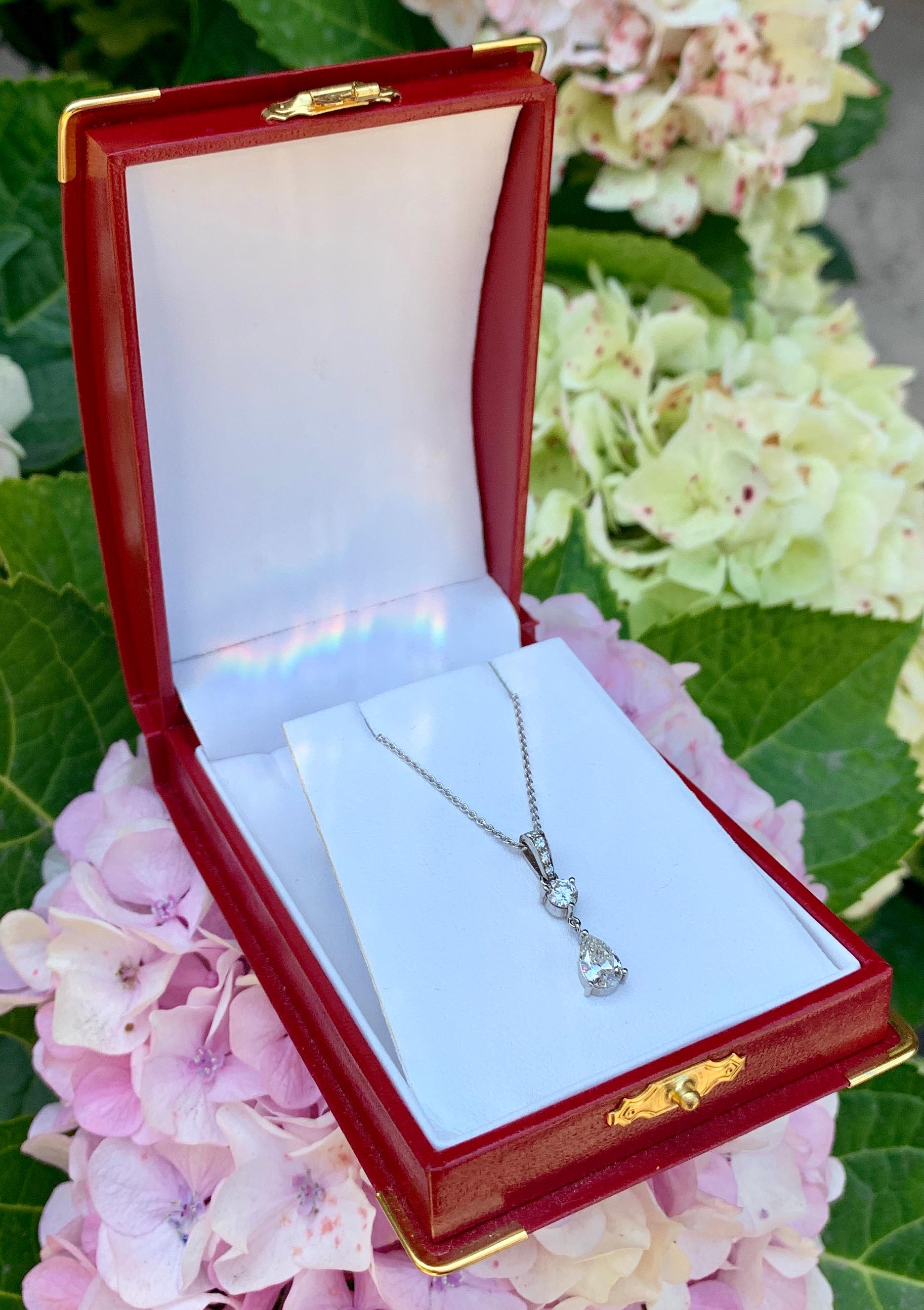 Segmented 14 karat white gold diamond estate pendant features a prong set pear cut diamond suspended beneath a prong set round brilliant diamond and attached to a bale embellished with 4 round brilliant diamonds which are pave set and accented with