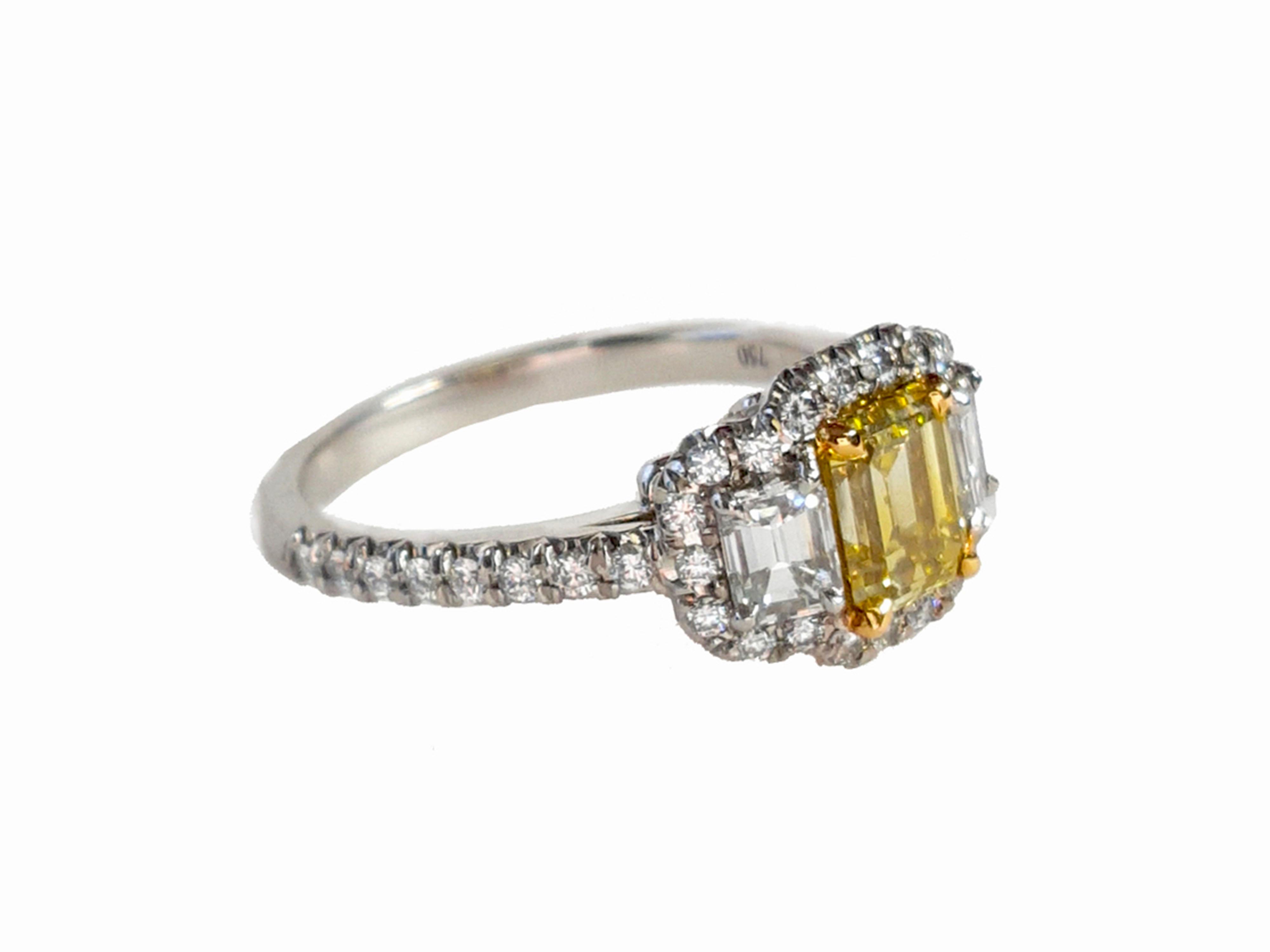 Ein atemberaubender Drei-Steine-Verlobungsring, 1,01 Karat Fancy Intense Yellow Emerald cut Diamant. Flankiert von zwei Diamanten im Smaragdschliff mit einem Gesamtgewicht von 0.51 Karat. Das klassische Design bringt die Schönheit des Mittelsteins