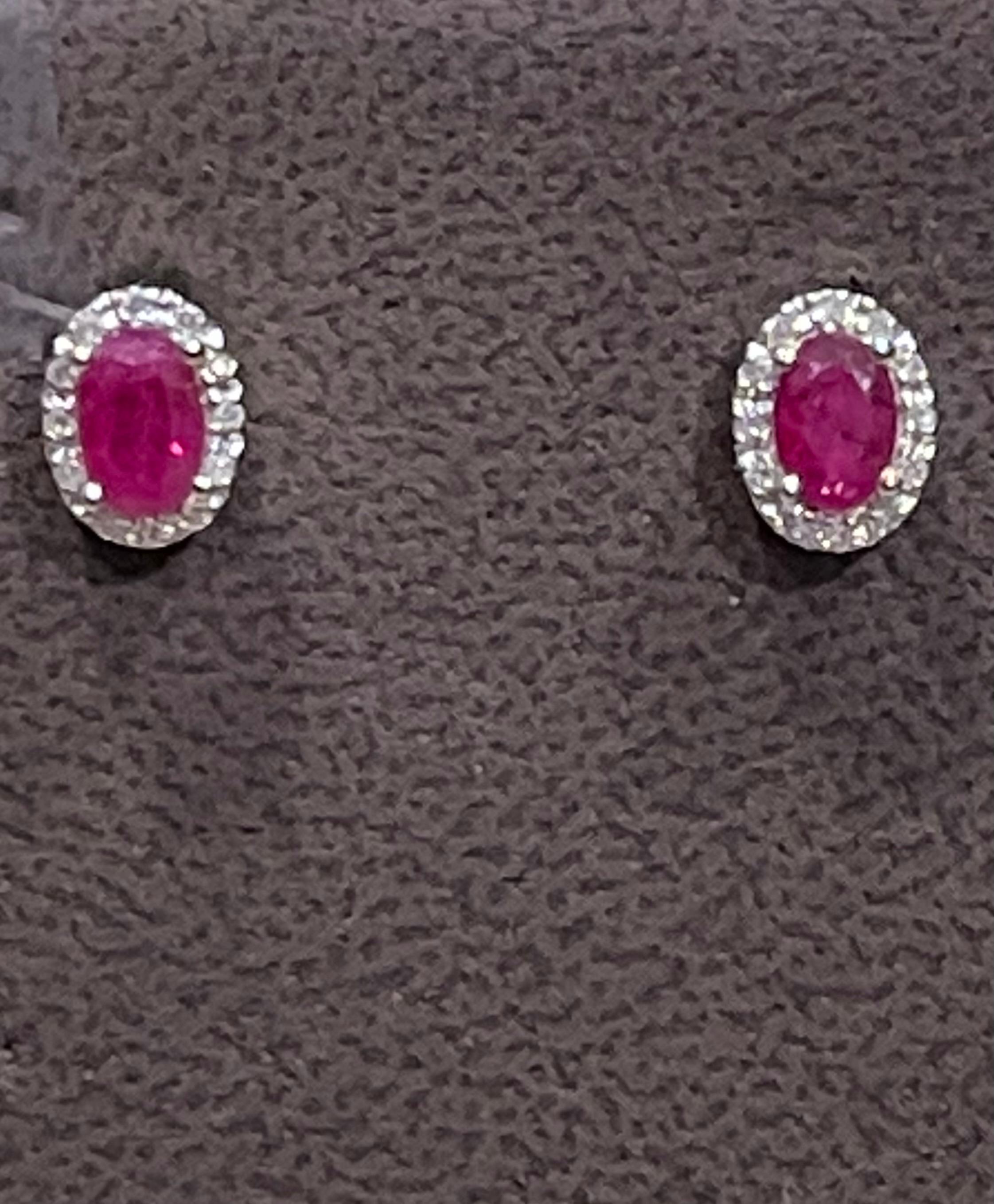 Cette luxueuse paire de clous d'oreilles en forme de halo de rubis est conçue en blanc 14 carats.  l'or. Les rubis rouges ovales sont entourés d'un éblouissant halo de diamants ronds.
 Boucles d'oreilles ovales en rubis naturel 14 carats  Blanc 