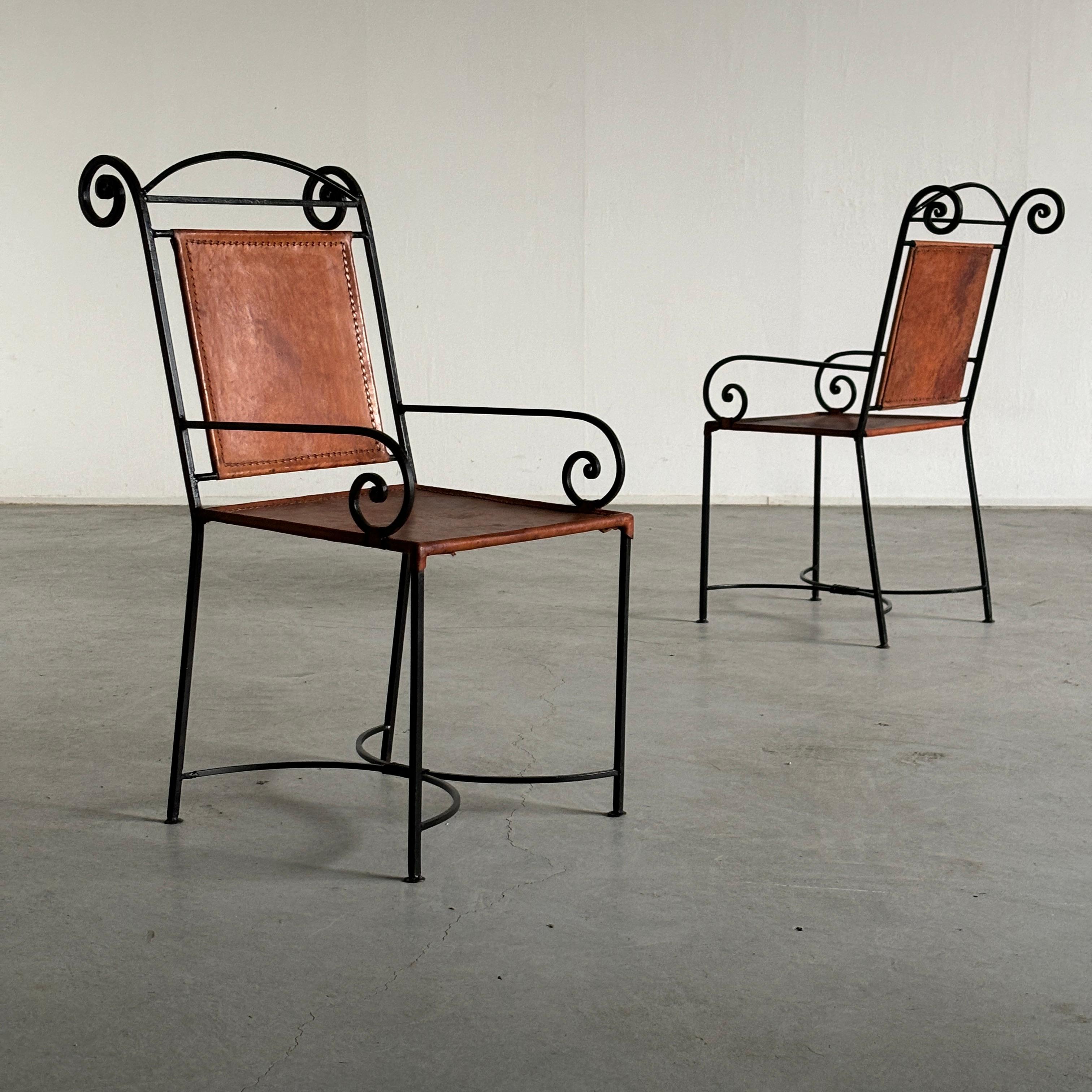Poltrone artigianali francesi vintage in stile mediterraneo. Composto da una struttura in ferro battuto nero che forma delle volute nelle sezioni dei braccioli e dello schienale. Sui telai poggiano spessi sedili e schienali in pelle cognac