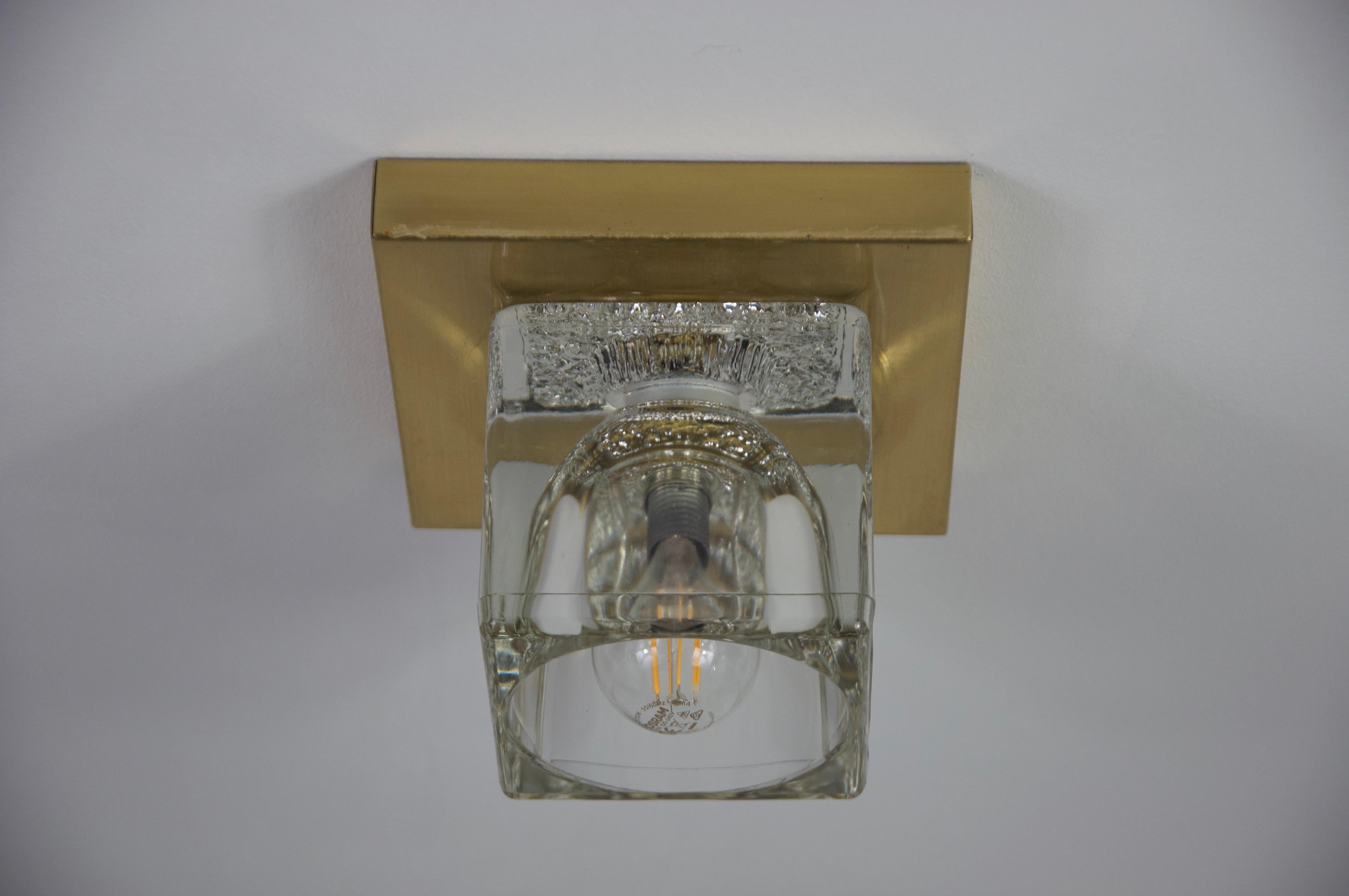 Questa elegante lampada degli anni '70 di Peill & Putzler è un pezzo versatile che può essere utilizzato sia come lampada da parete che da soffitto. Caratterizzata da una solida base in ottone e da un sorprendente paralume in vetro color ghiaccio,