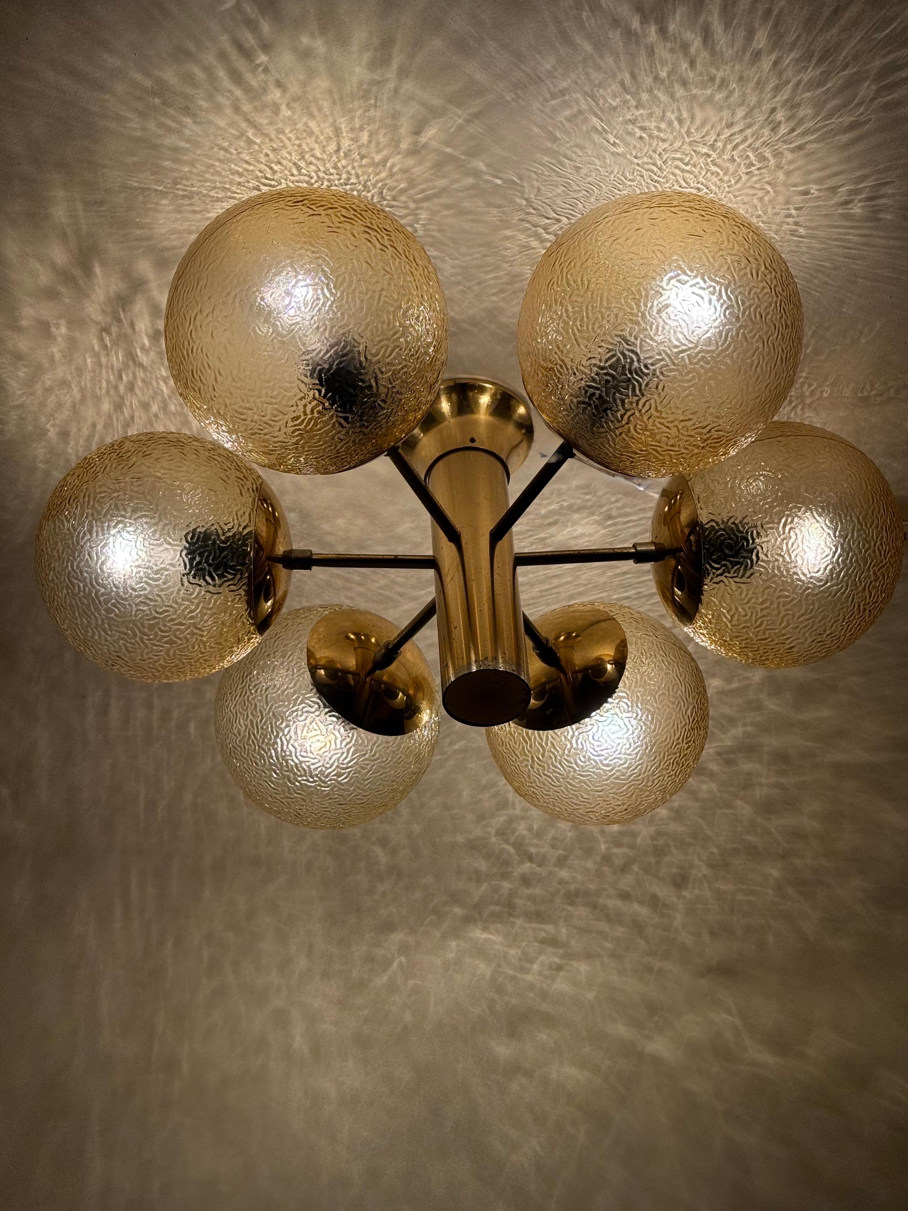 Ces magnifiques lustres provenaient à l'origine d'une salle de danse des années 1960, où ils étaient encore accrochés récemment. Les sphères en verre texturé ont une belle teinte ambrée dorée et leur motif texturé est exquis et attrayant. Ils sont