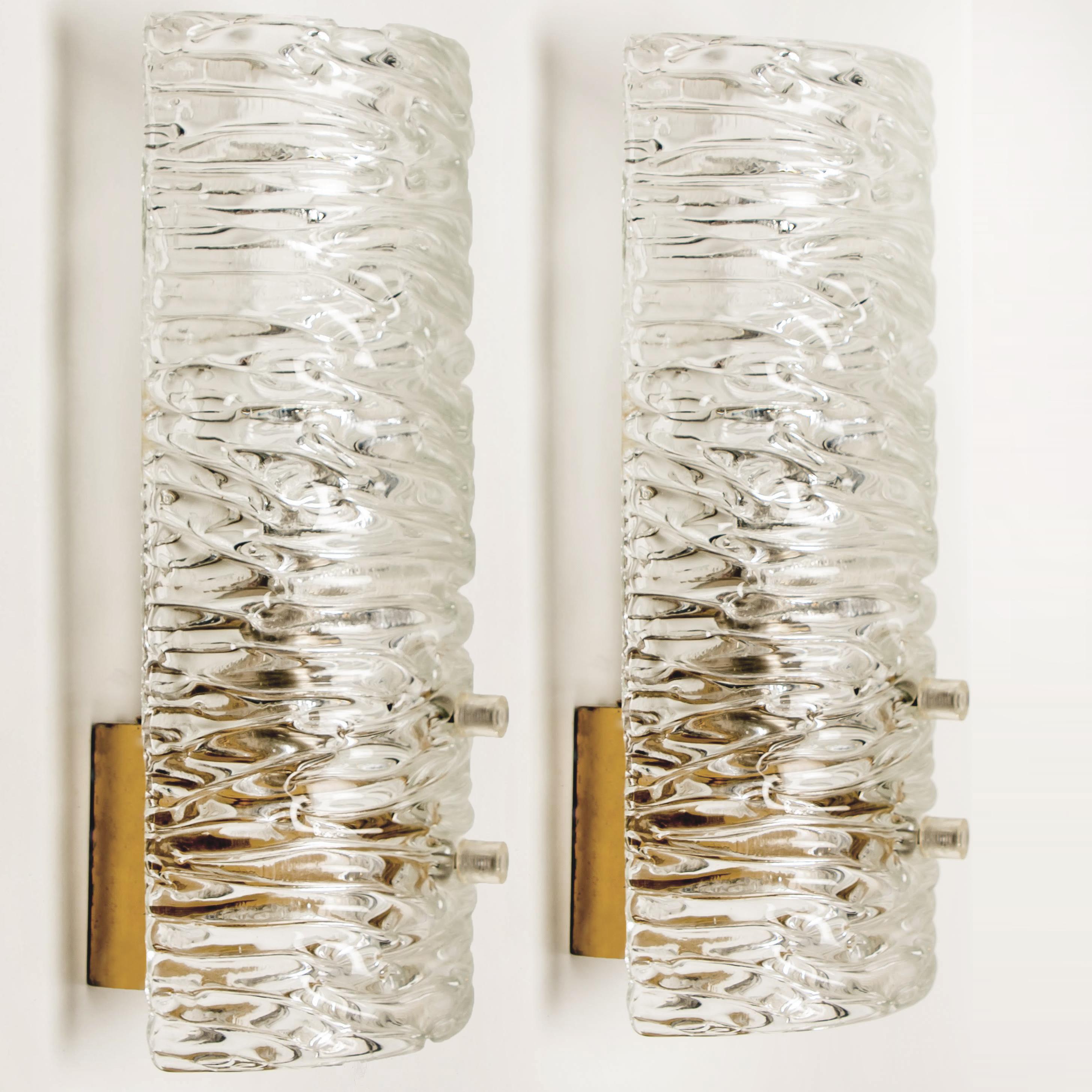 Two wall lights by J.T. Kalmar, Vienna, Austria, manufactured in circa 1960. This pair is handmade and high end. Each wall light has a half round wave textured glass shade with a brass back plate,

The wave texture gives a nice diffuse light