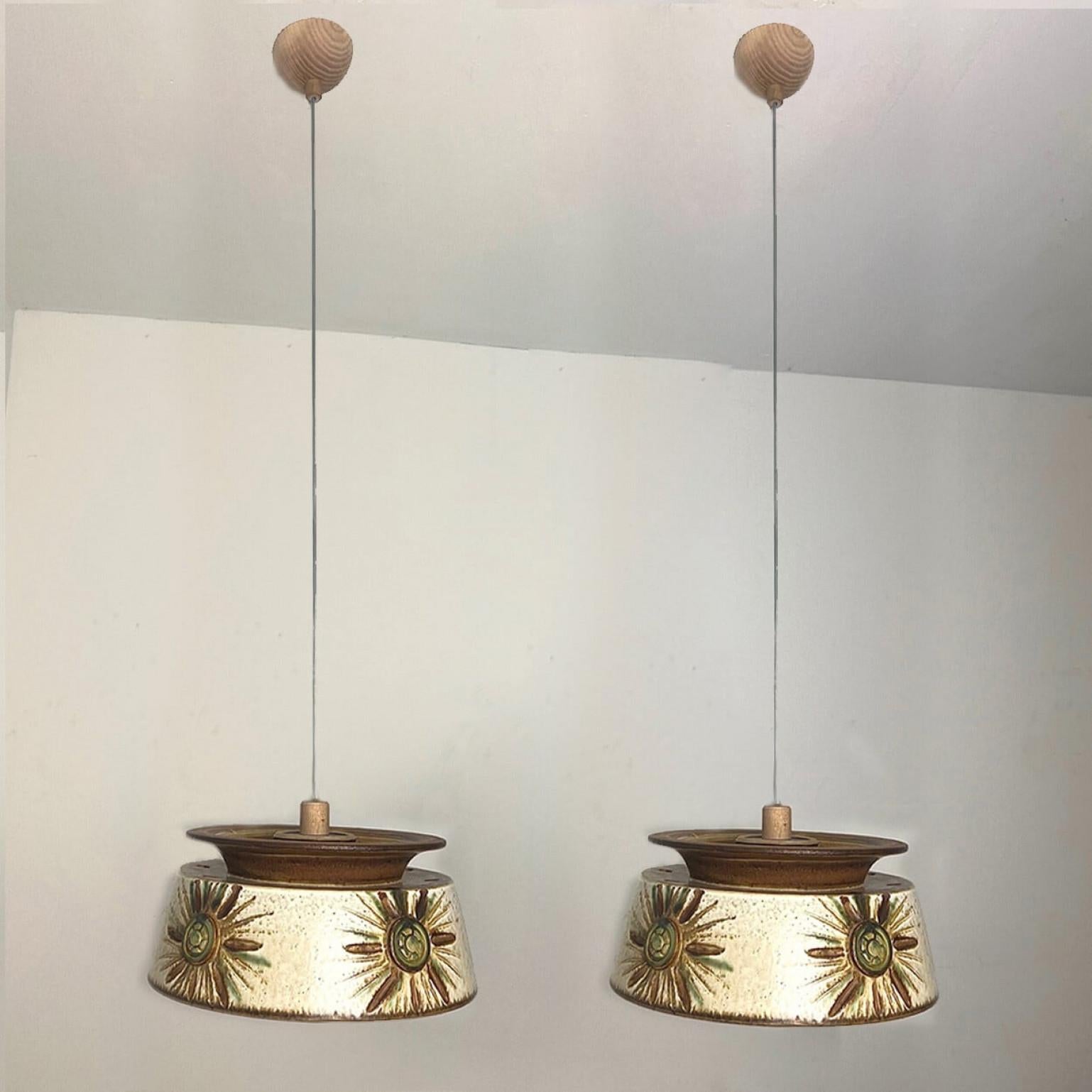 Una delle due splendide lampade a sospensione rotonde dalla forma insolita, realizzate in ceramica blu, verde, beige e marrone, prodotte negli anni '70 in Danimarca.

Con bellissimi e fragili cavi d'acciaio e dettagli in legno. Appesi a un cavo