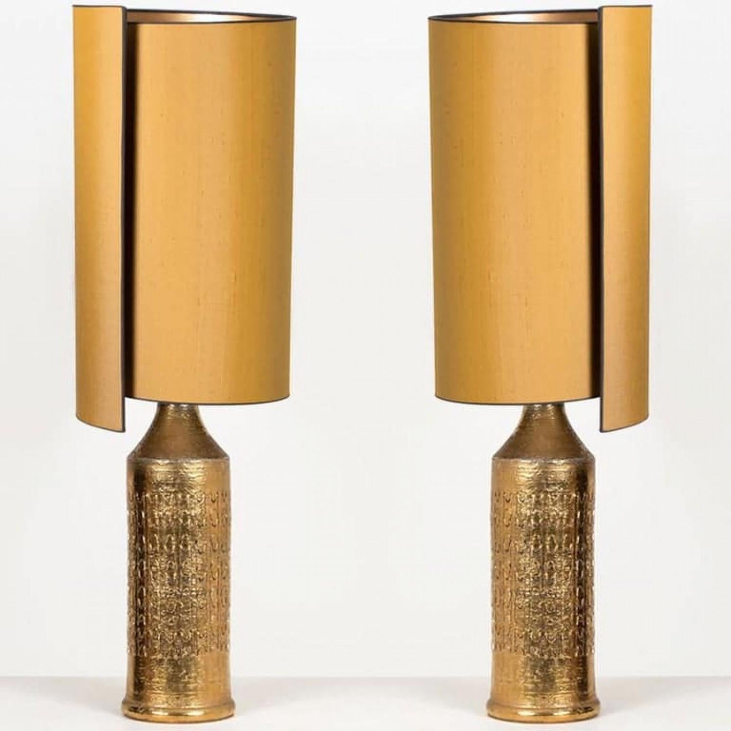 1 de las 2 elegantes lámparas de mesa. Cada lámpara tiene una base de cerámica con una superficie rugosa en un esmalte blanquecino con brillantes dibujos metálicos dorados, Bitossi, Italia, hacia la década de 1960. Con nuevas y excepcionales